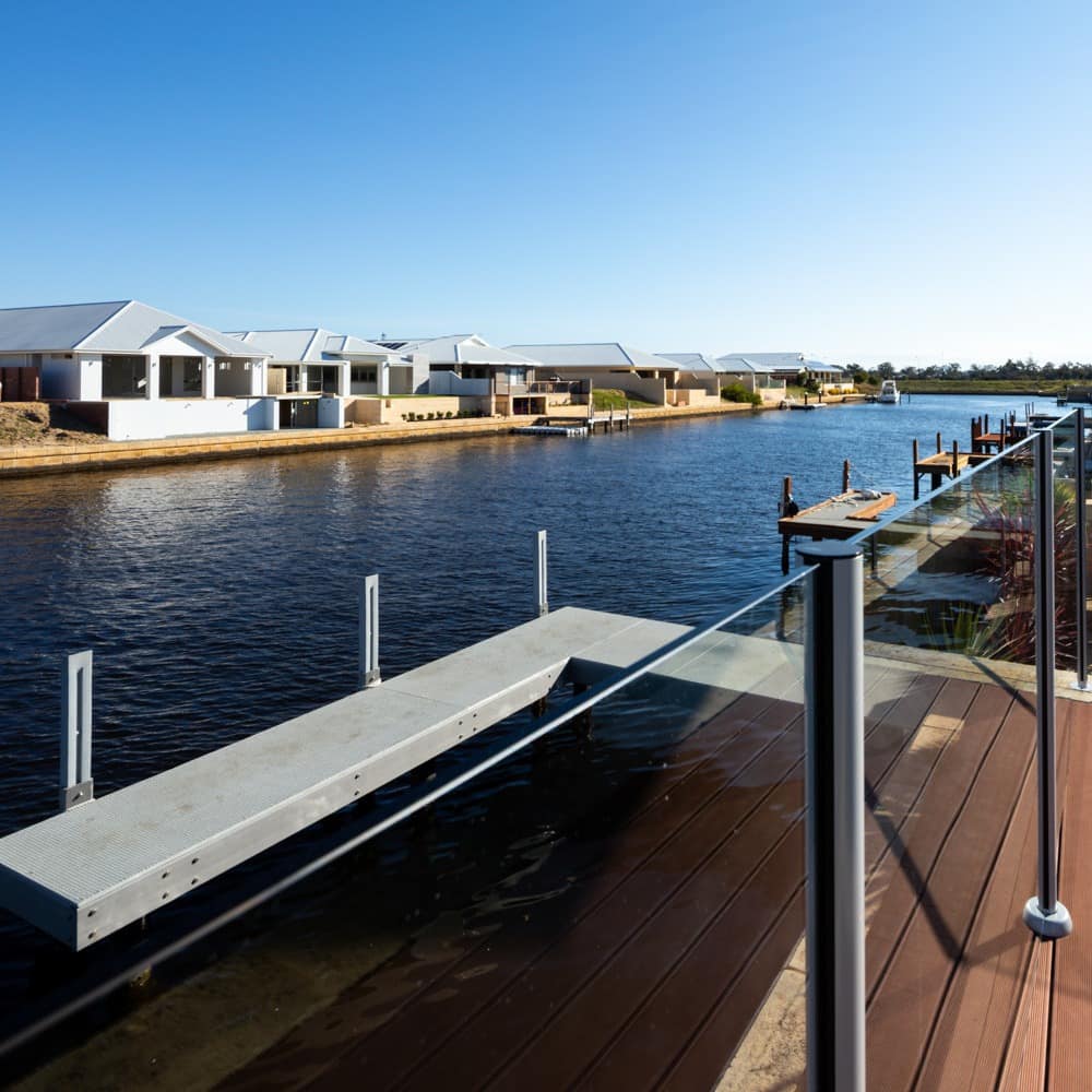 Glass-walled balcony and dock of a home on the canal with deep blue waters and other waterfront homes in the distance.