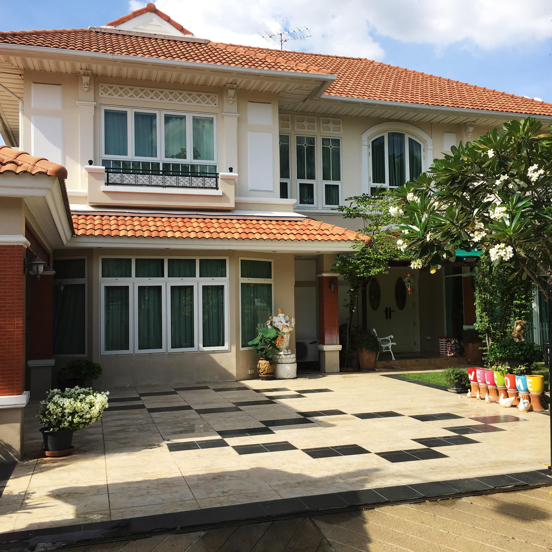 A large elegant home with beige and white siding and spanish tile roof, beige and black tile driveway, a lush front lawn.