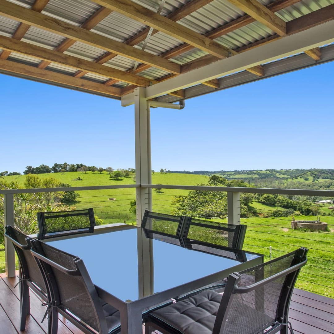 Porch of farm house with railings and seating area overlooking lush garden