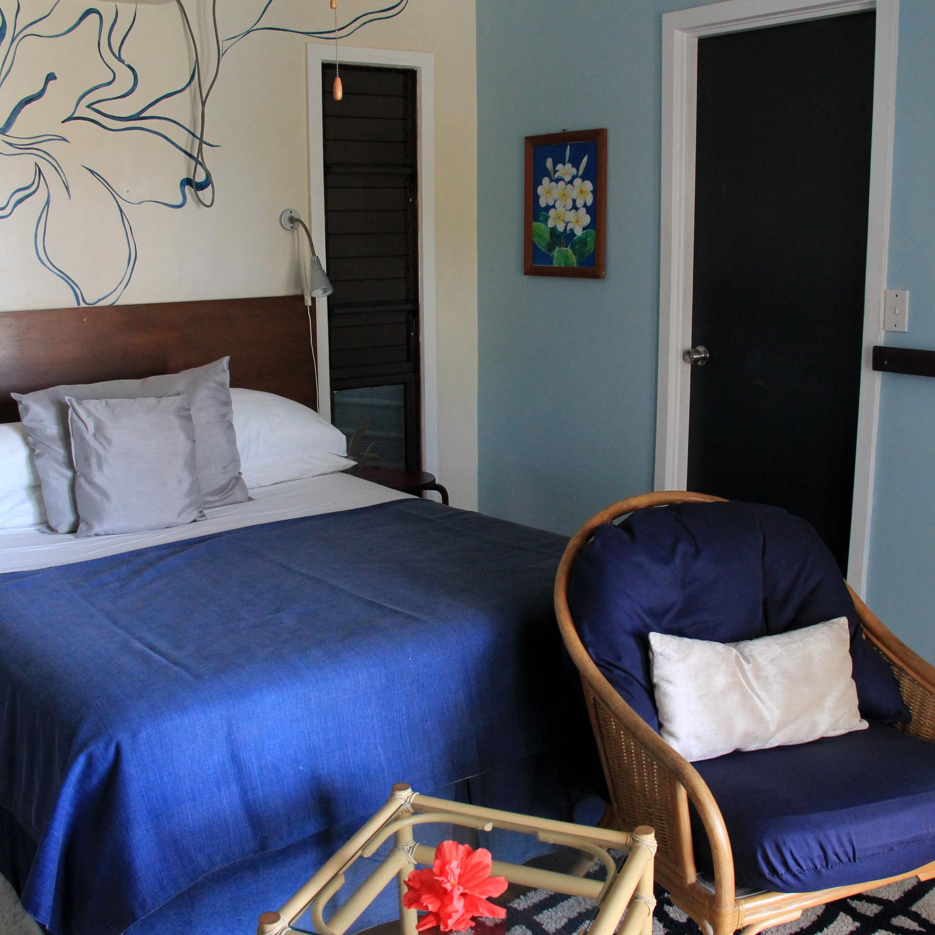 A bedroom with light blue walls and a flower mural, a king size bed, white and blue bedding, and bamboo decor.