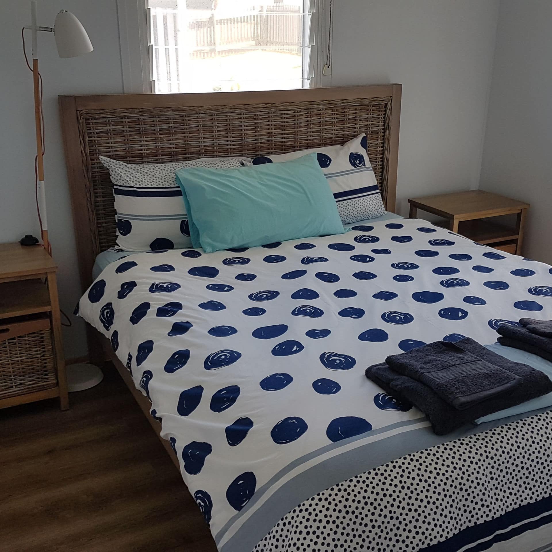 Bedroom with hardwood floors, white walls, wicker framed queen size bed with blue and white bedding.