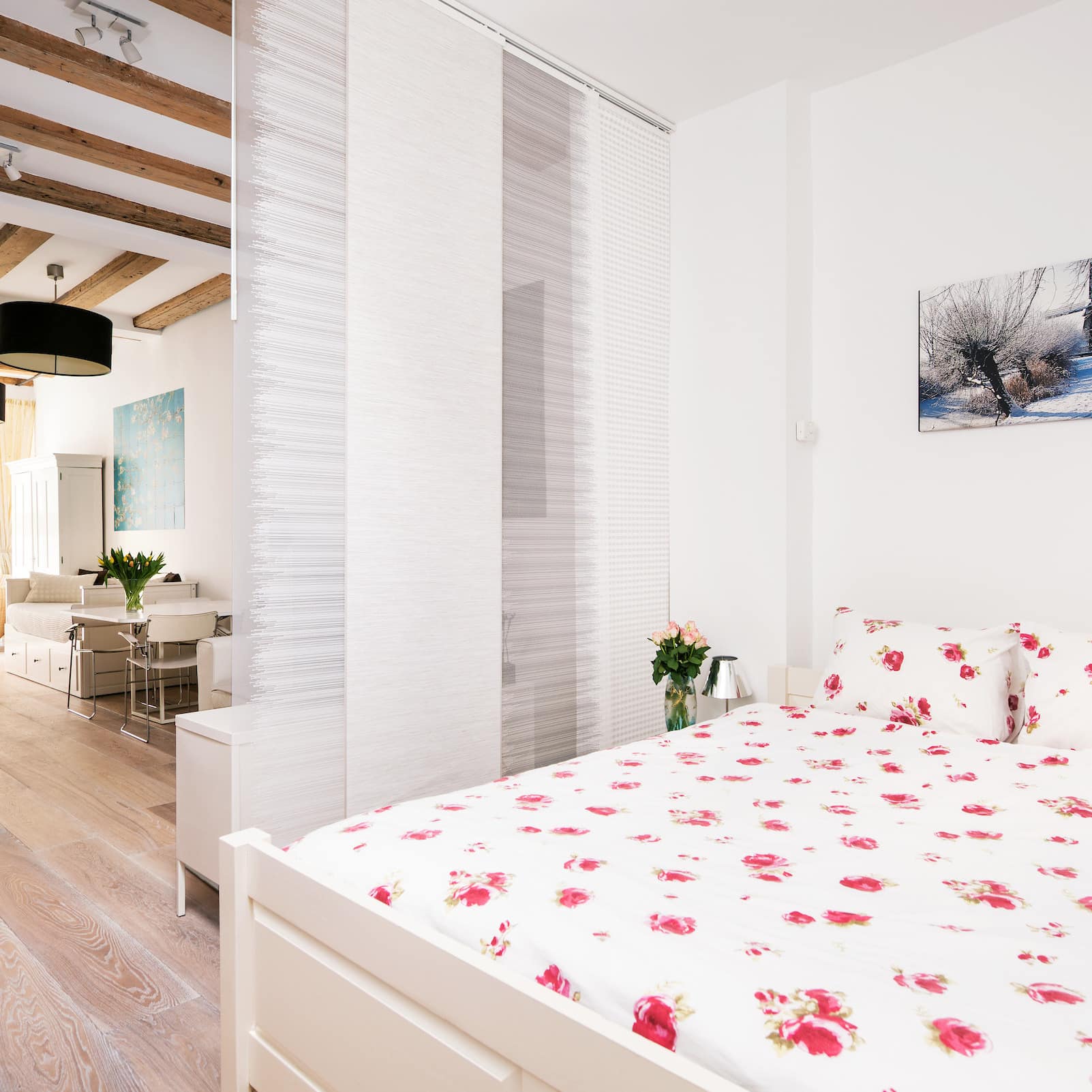 King-sized bed in open Amsterdam apartment with whitewashed wood floors, 50’s-style American kitchen and living area