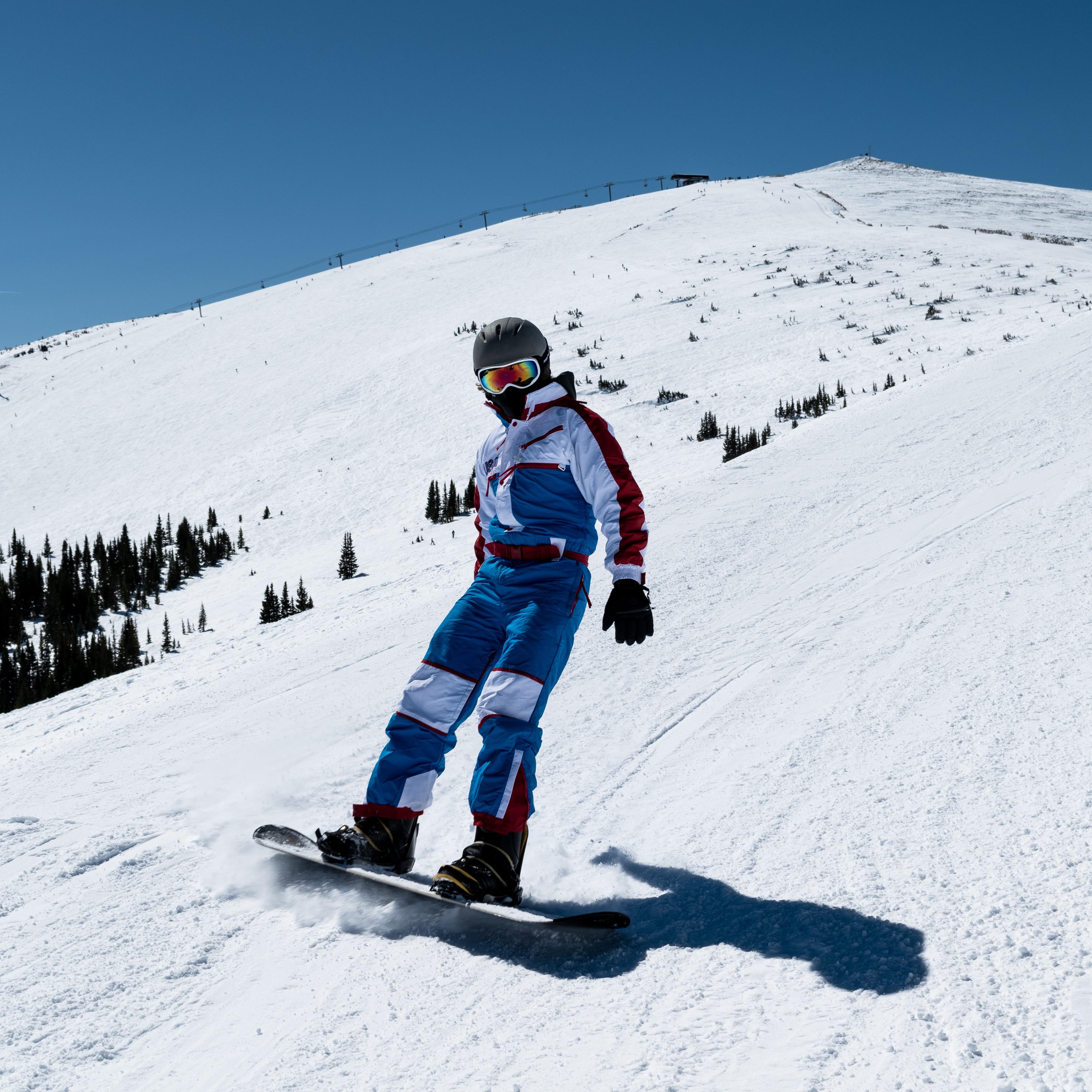 Person snowboarding down the side of a snowy mountain with trees dotting the side
