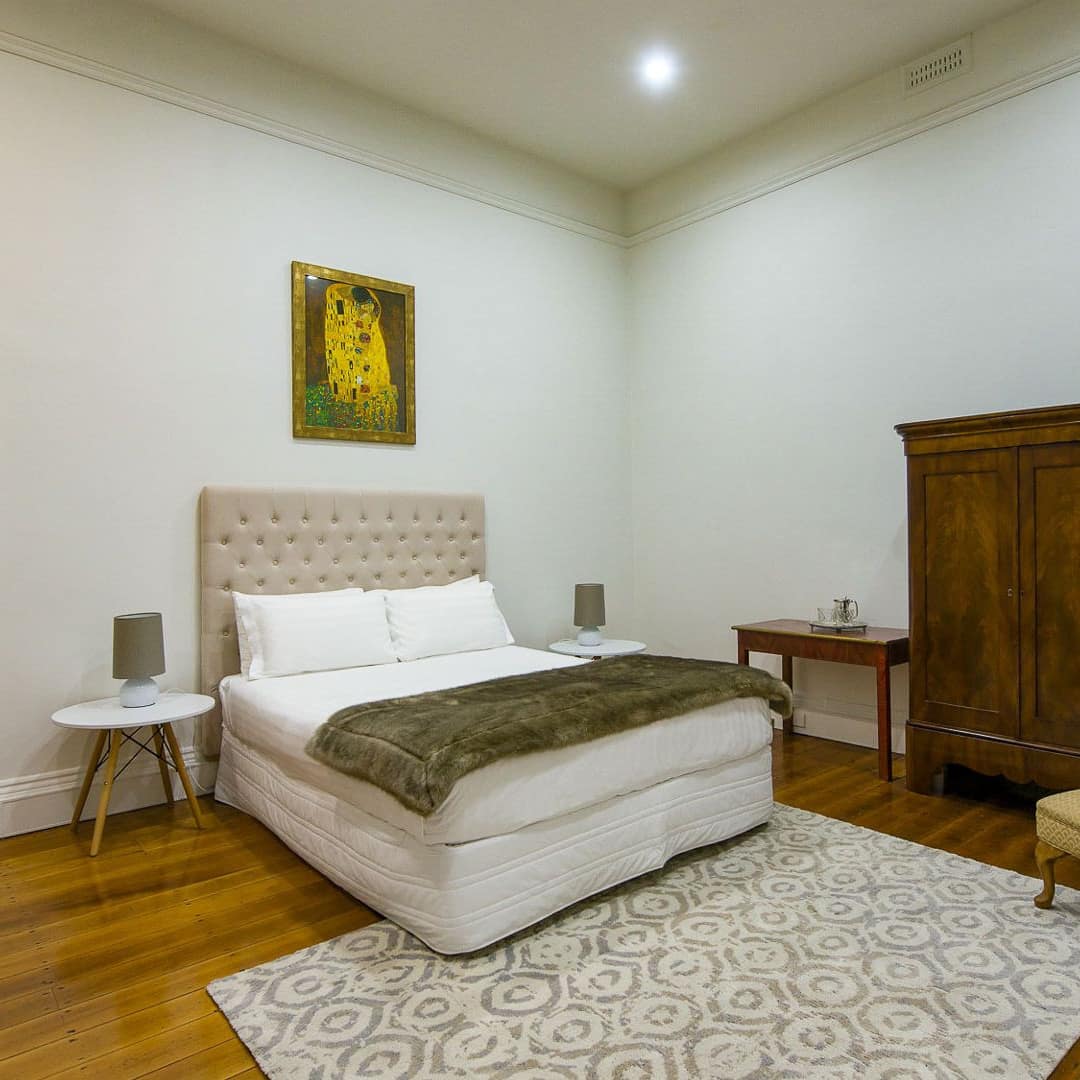 Spacious bedroom with hardwood floors, white walls, a king size bed, white bedding, and antique decor.