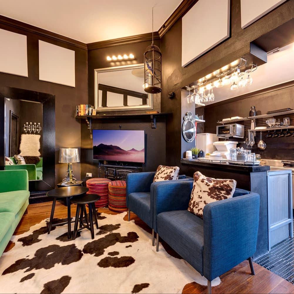 Eclectic living room with hardwood floors, black walls, blue and green furniture, cowhide rug, and full kitchen.