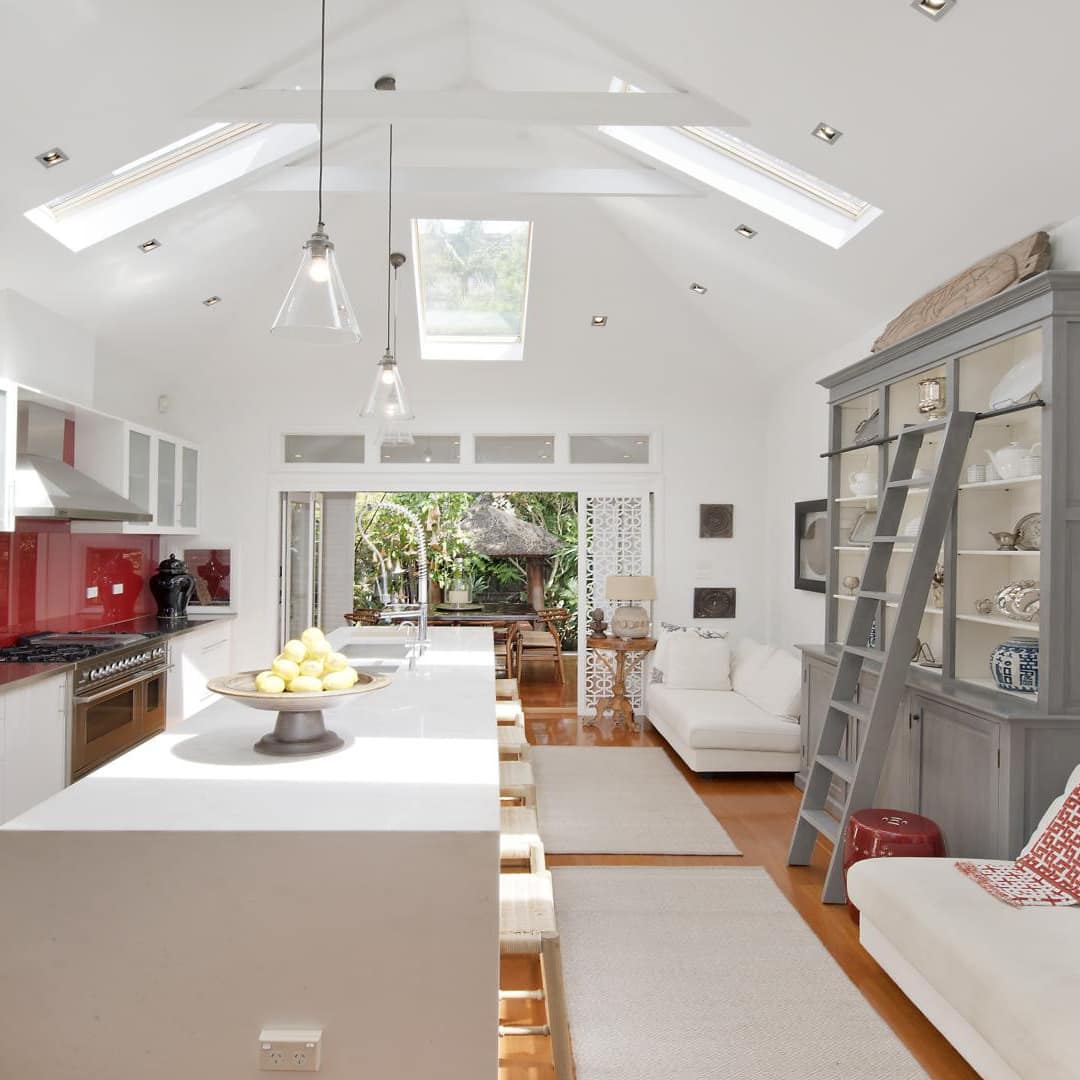 Open living and dining area with white kitchen breakfast bar, grey china cabinet, white sofa and red-accented kitchen