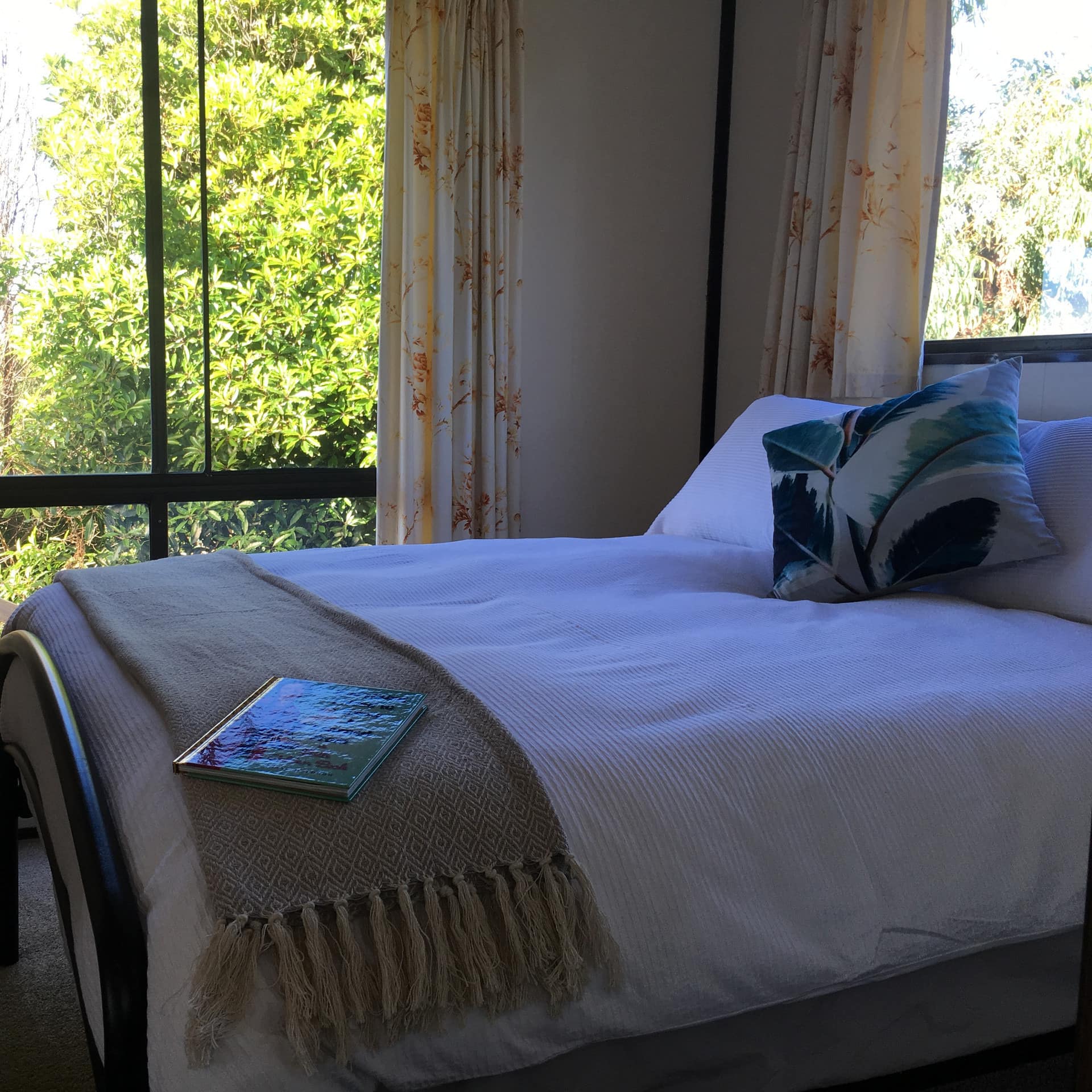 Charming bedroom with a black metal king-size bed, white and tan bedding, tall windows with yellow floral curtains.