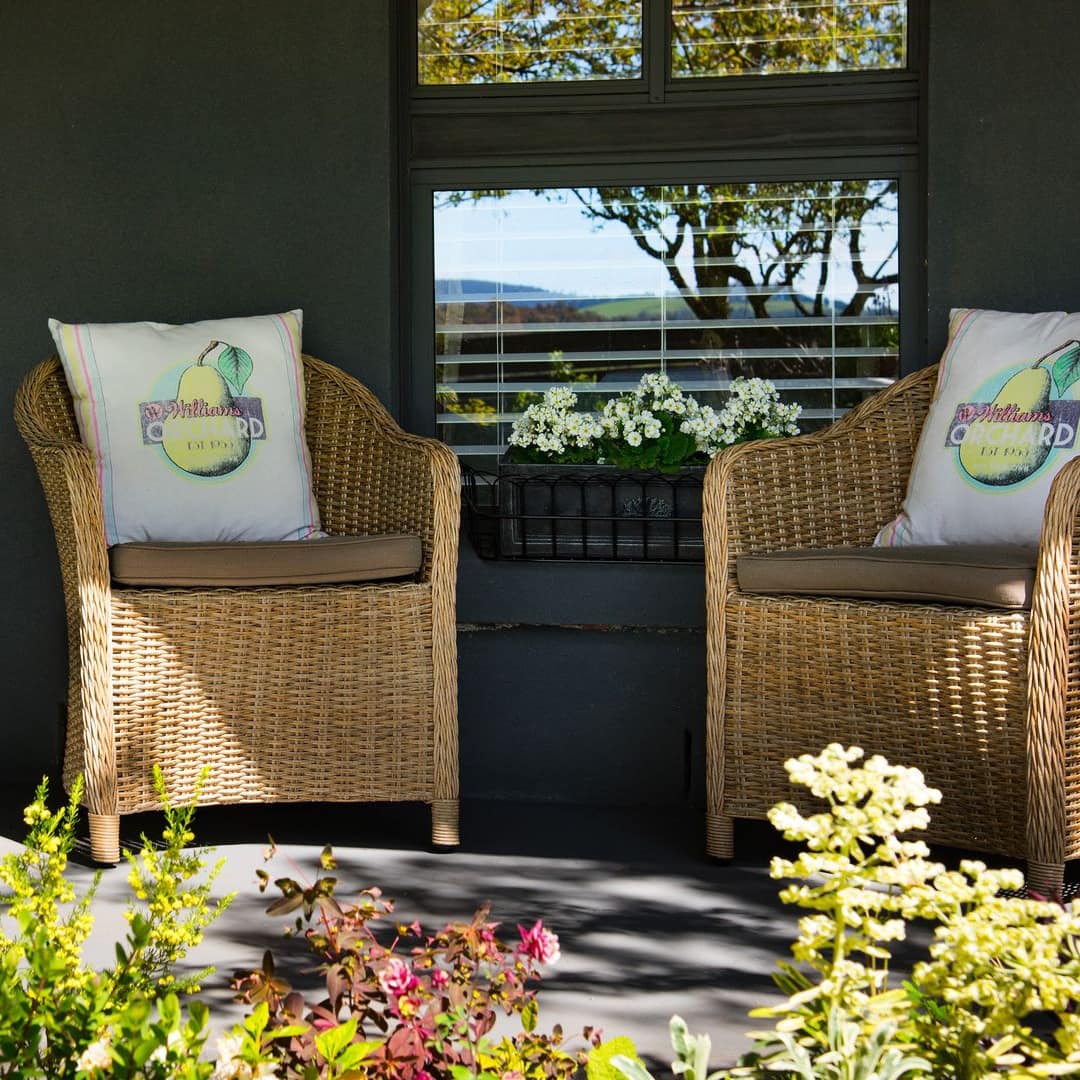 Sunny porch with black siding, two wicker chairs, and lush greenery.