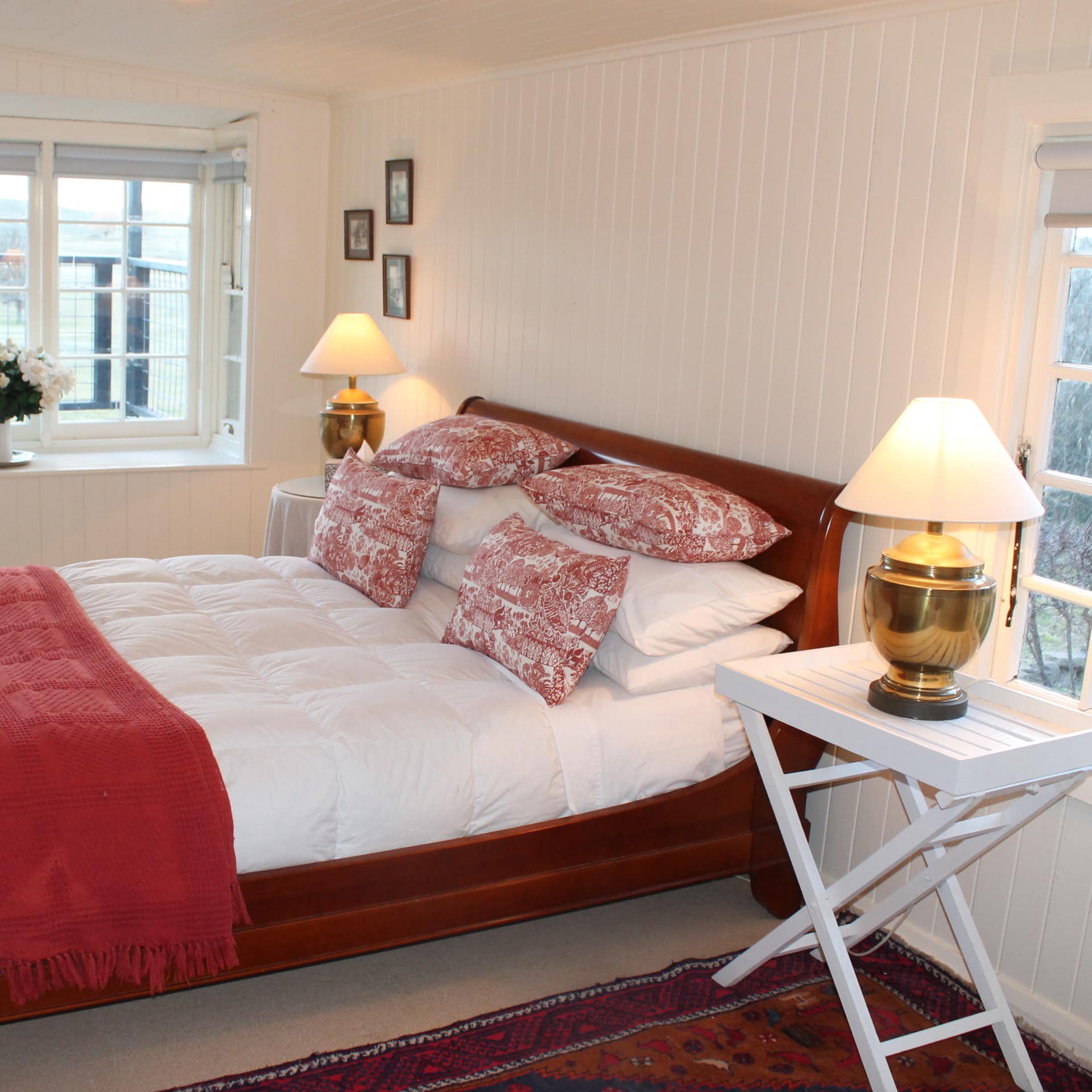 White bedroom with cherry-wood sleigh bed, white down bedding, red toile pillows, red blanket, wide recessed window.