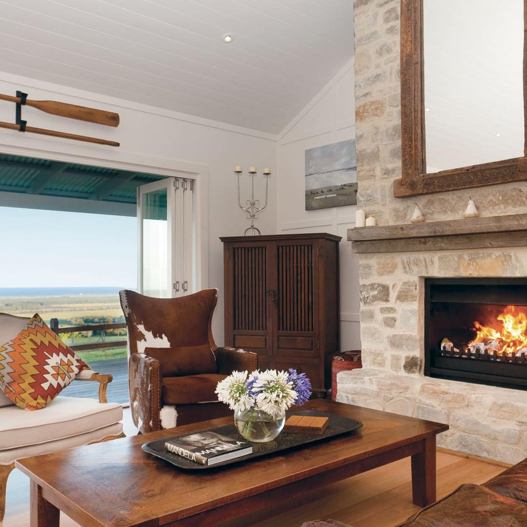 Open living room with hardwood floors, natural stone fireplace, farmhouse decor, and glass accordion patio doors.