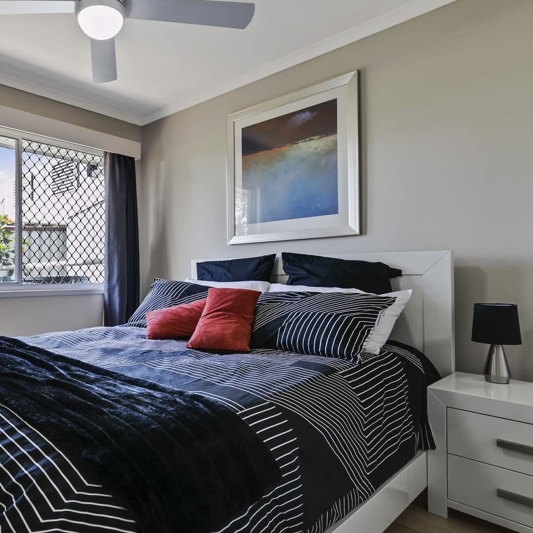 A bedroom with hardwood floors, grey walls, a king size bed with black and white bedding, and wide windows.