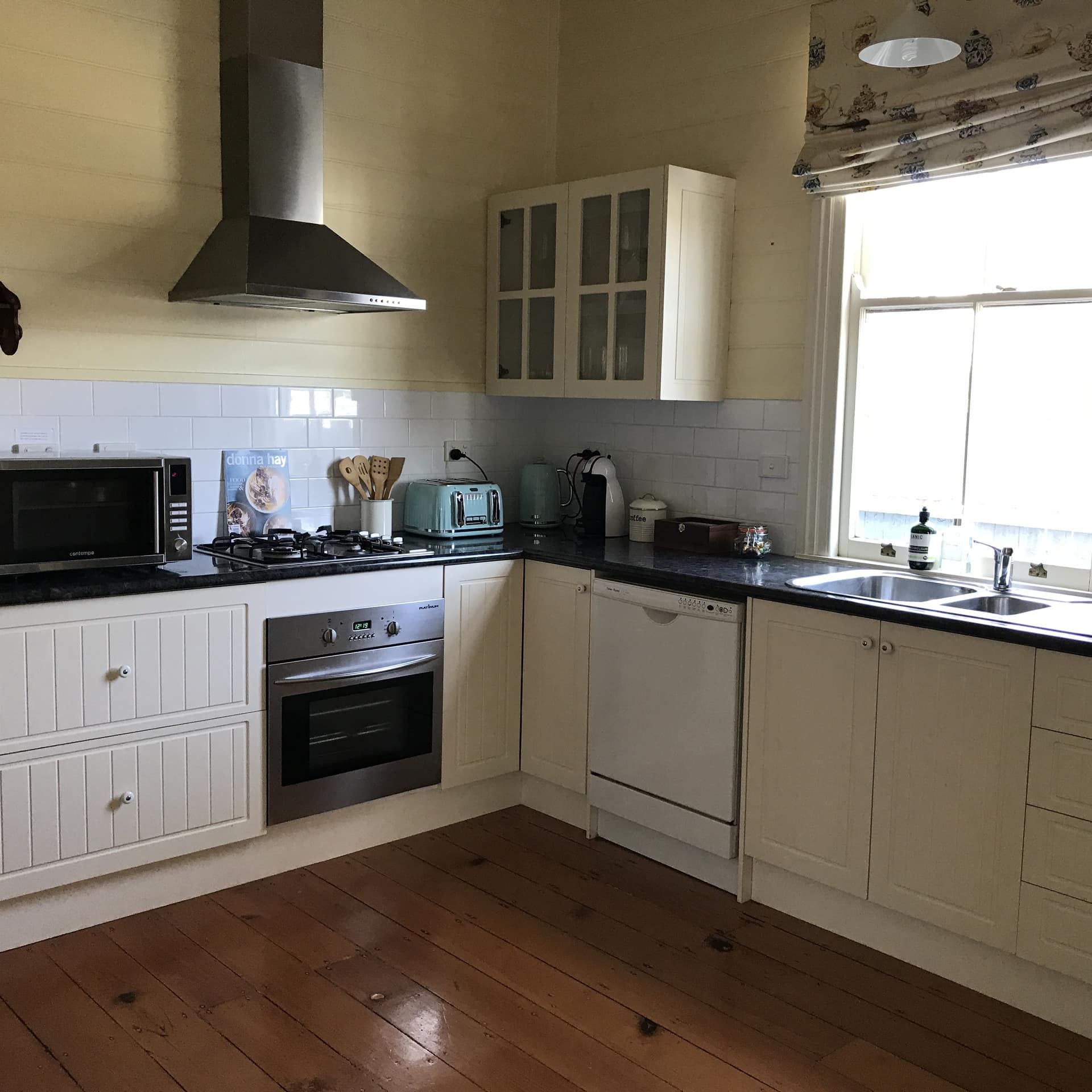 Cottage kitchen with cream cabinets, black granite countertop, gas range, hardwood floors and a sunny window over the sink.