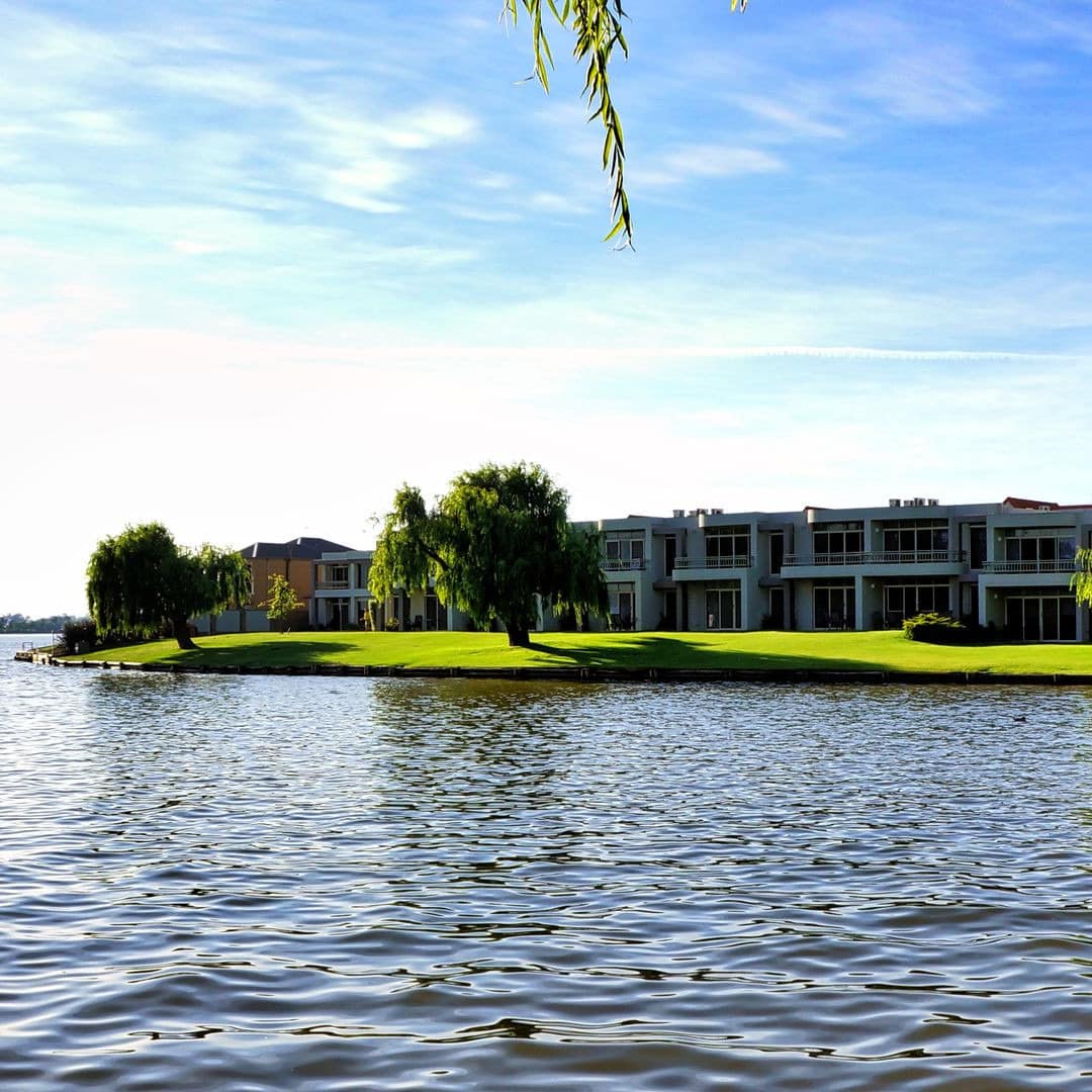 Lake Mulwala in the foreground of an apartment building set on a green lawn with trees