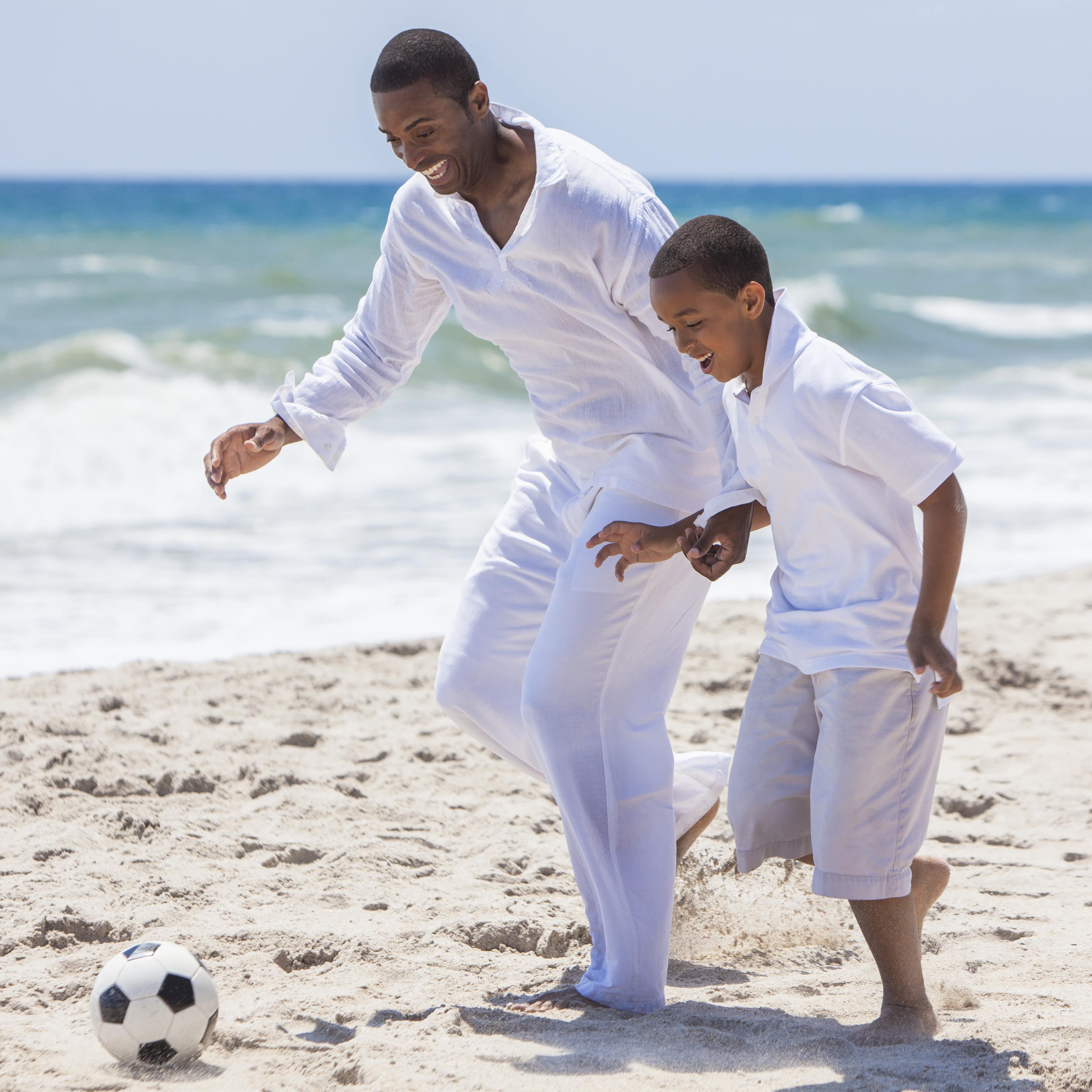 Father and son playing football on the beach