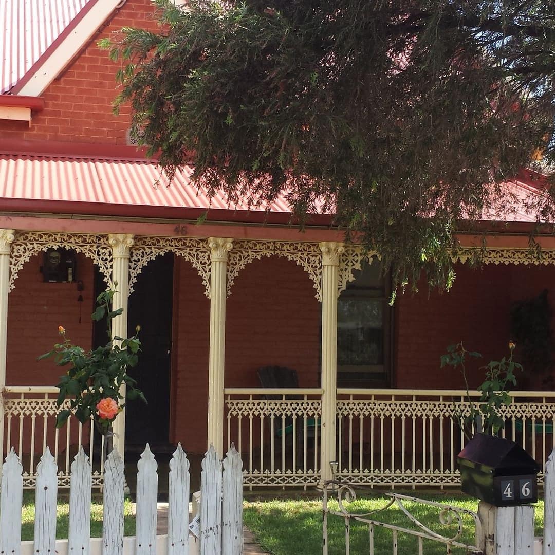Historic, brick cottage with red roof, white porch railings, white picket fence, and a lush front lawn.