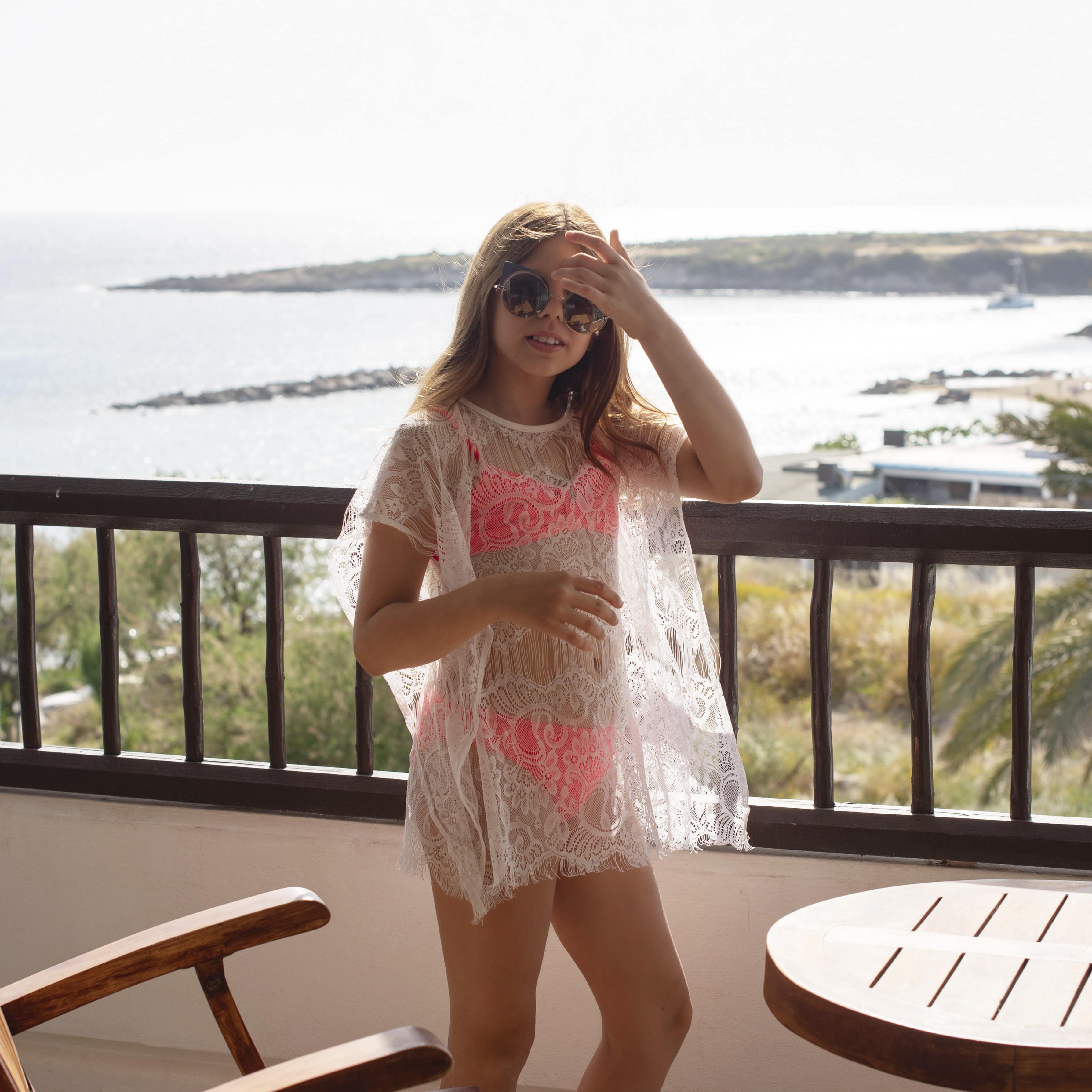School aged girl with sunglasses on balcony of apartment with ocean in the background