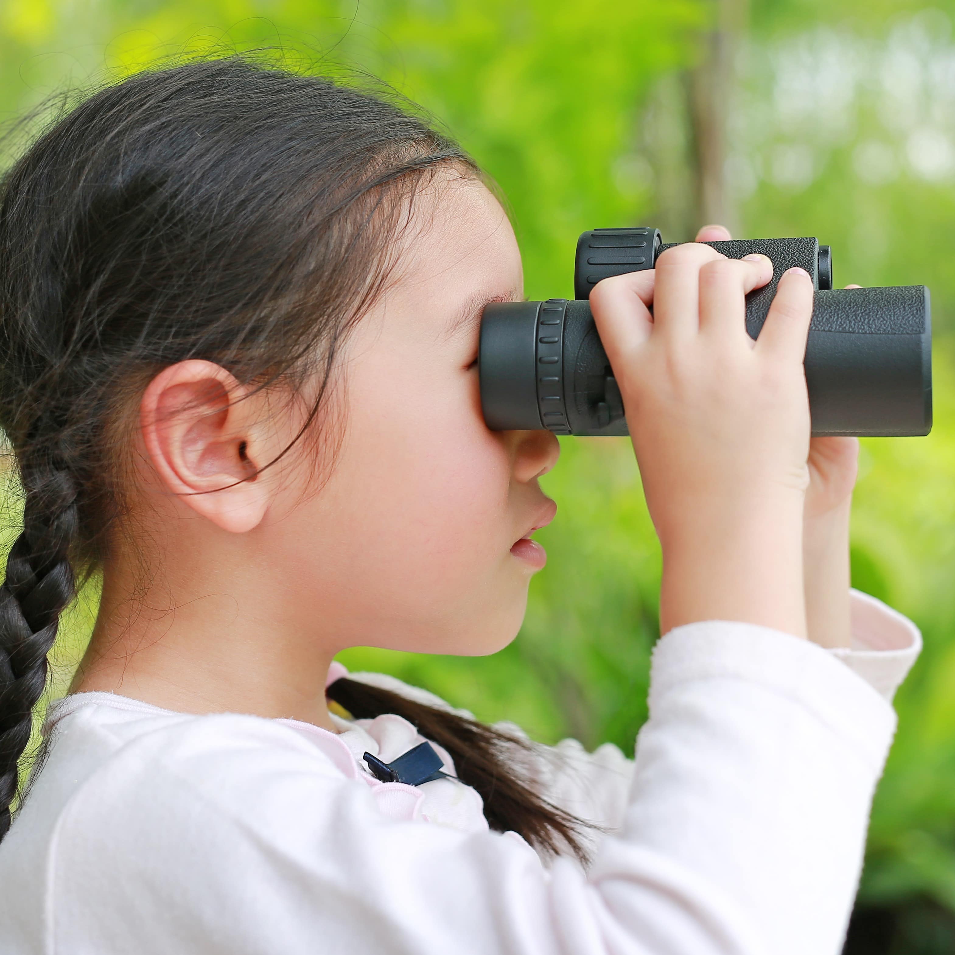Young girl in on trail in trees looking through binoculars
