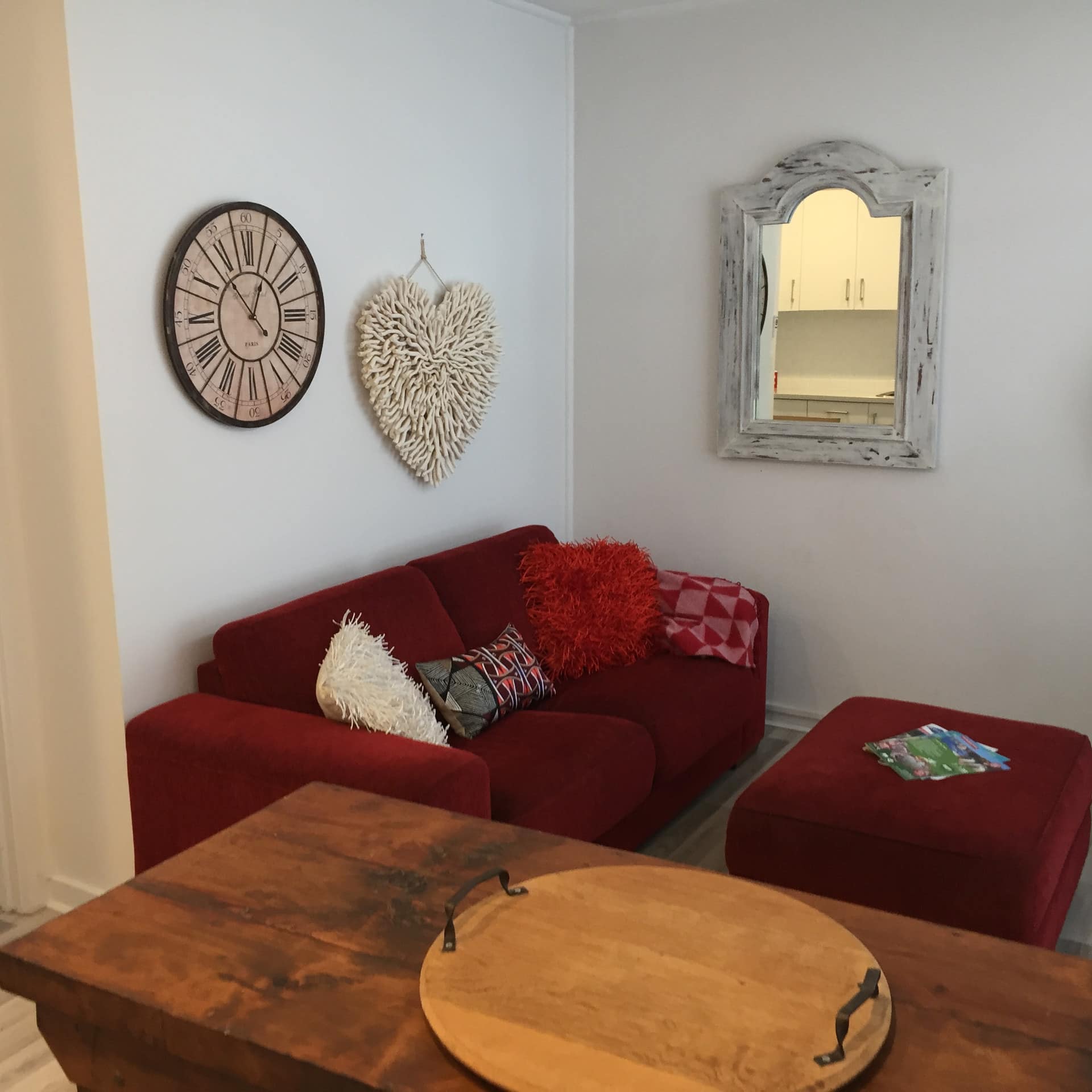 Living room of 1-bedroom cosy beach apartment with red cloth sofa lined with pillows