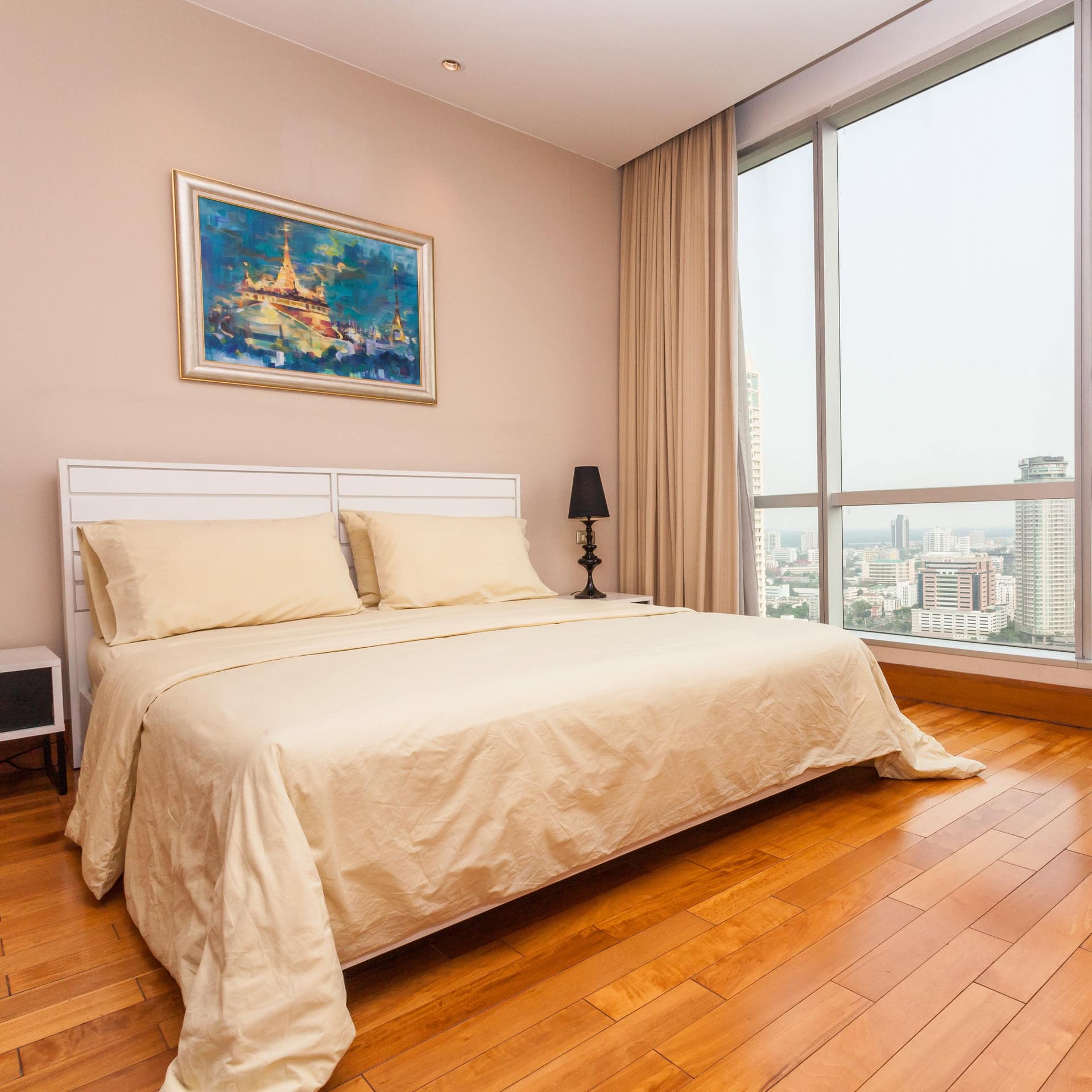 Spacious bedroom with hardwood floors, a king size bedroom, beige bedding, a desk, floor to ceiling windows with city views.