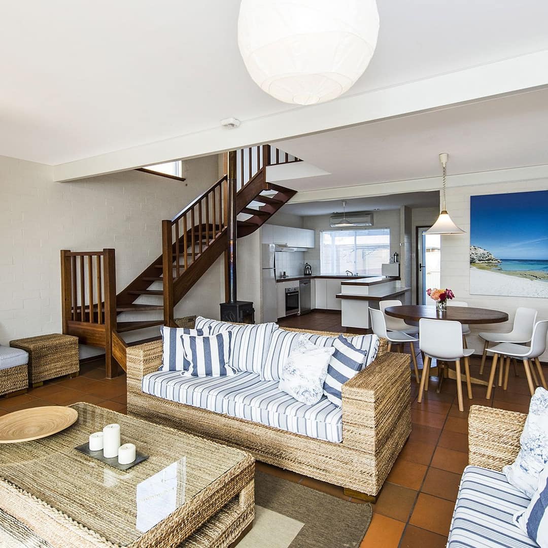 An open living and dining room with orange tile floors, matching wicker sofas and coffee table, and a wooden dining set.