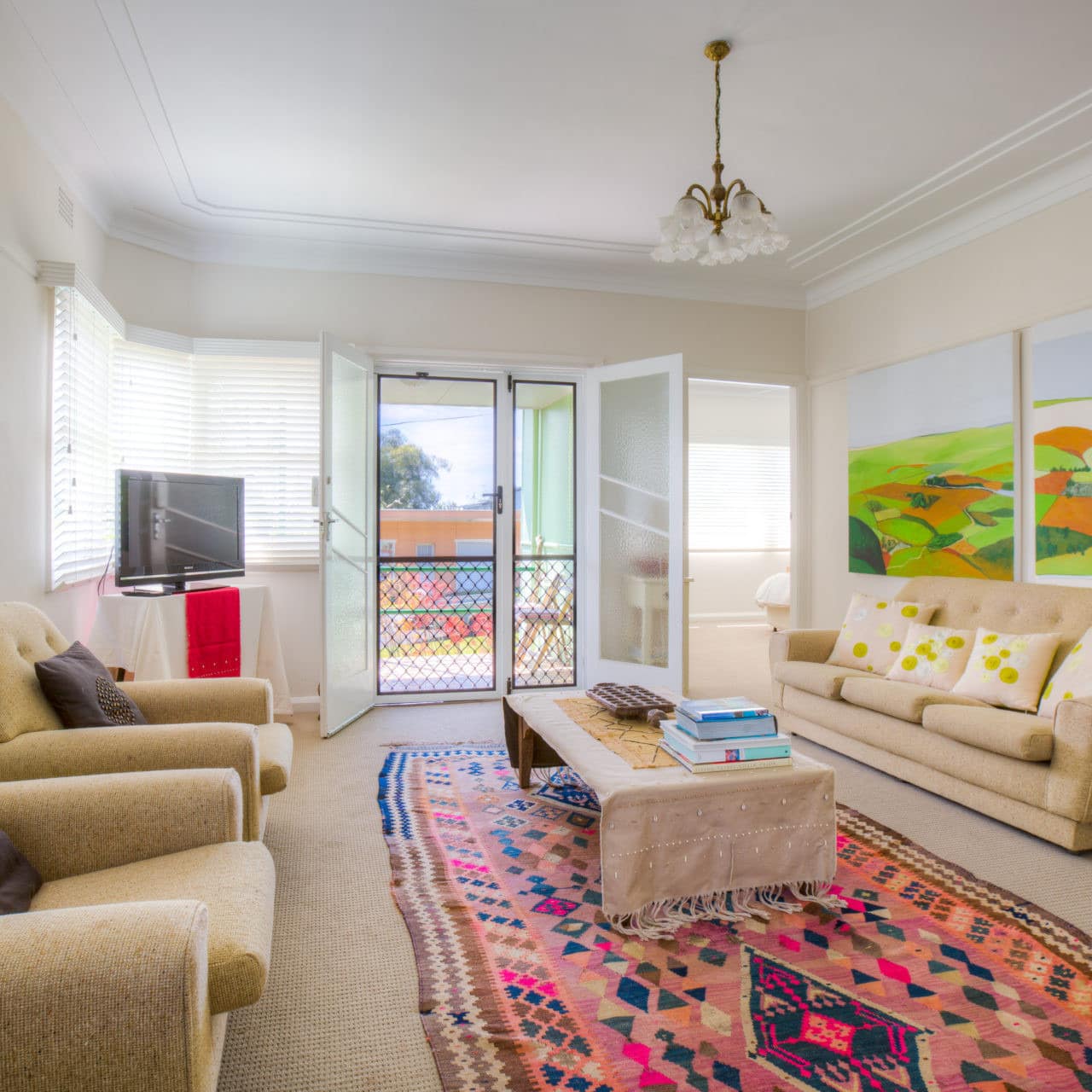 Living room of two-bedroom beach cottage with soft cloth sofa and overstuffed chairs with colourful Persian rug