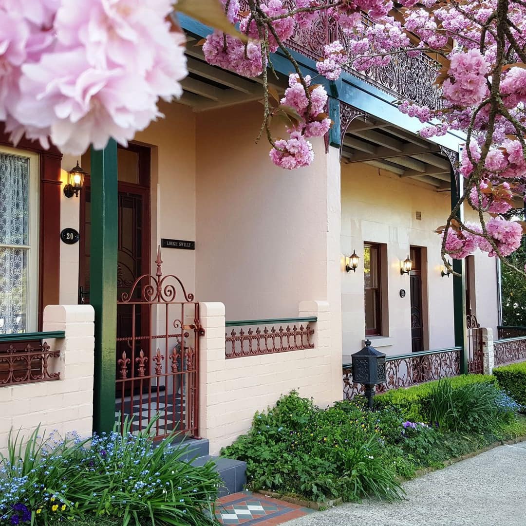 Two-storey 1885 Victorian Terrace with peach-coloured brick and plaster, wrought-iron railings, garden, and cherry trees.