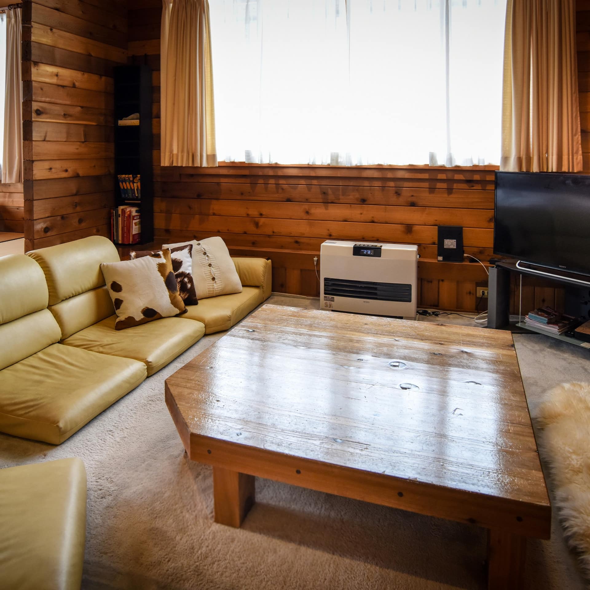 A wood-panelled sunken living room with a low coffee table, yellow leather floor cushions, and wide windows.