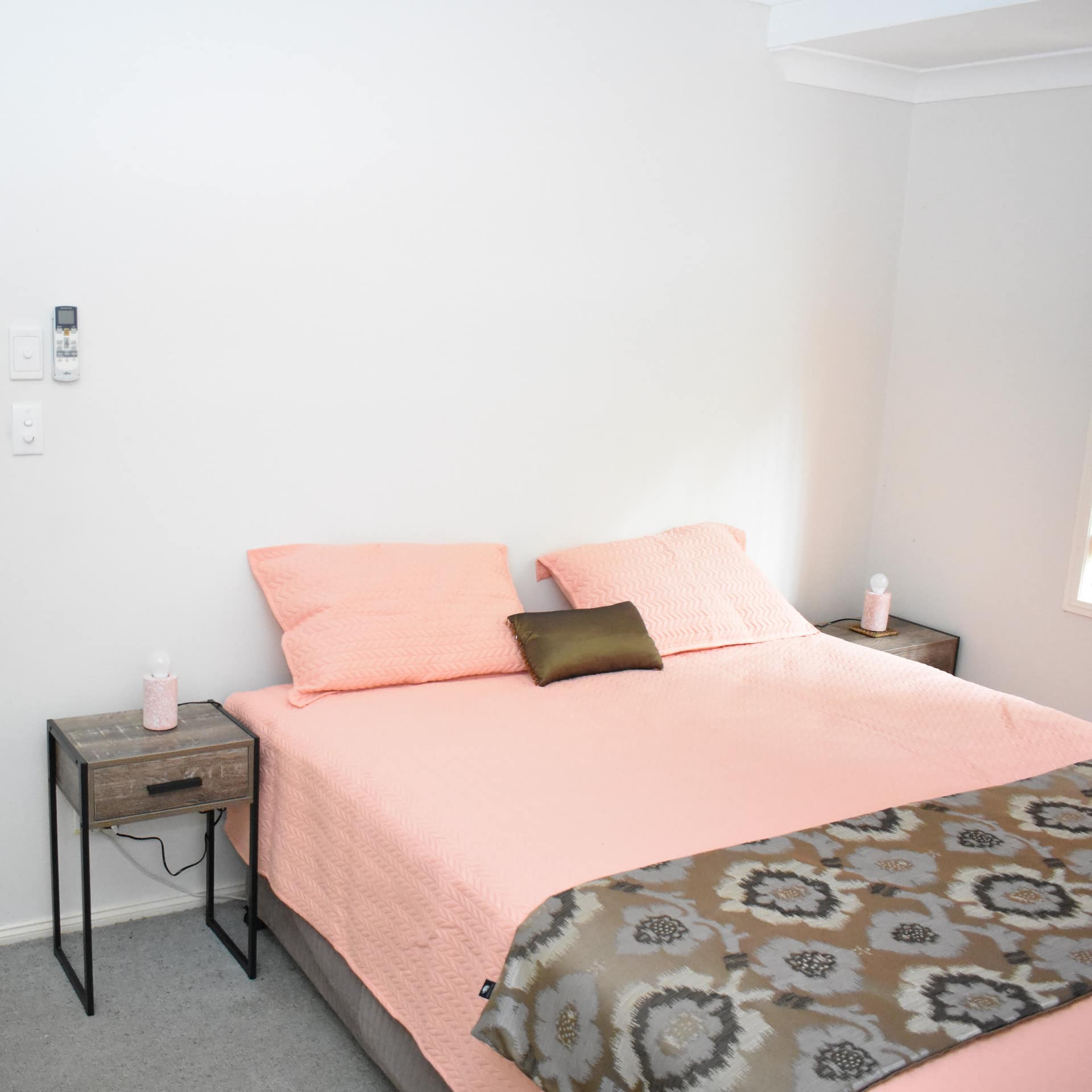 Bedroom with grey carpet, white walls, and a king size bed with pink and brown bedding.