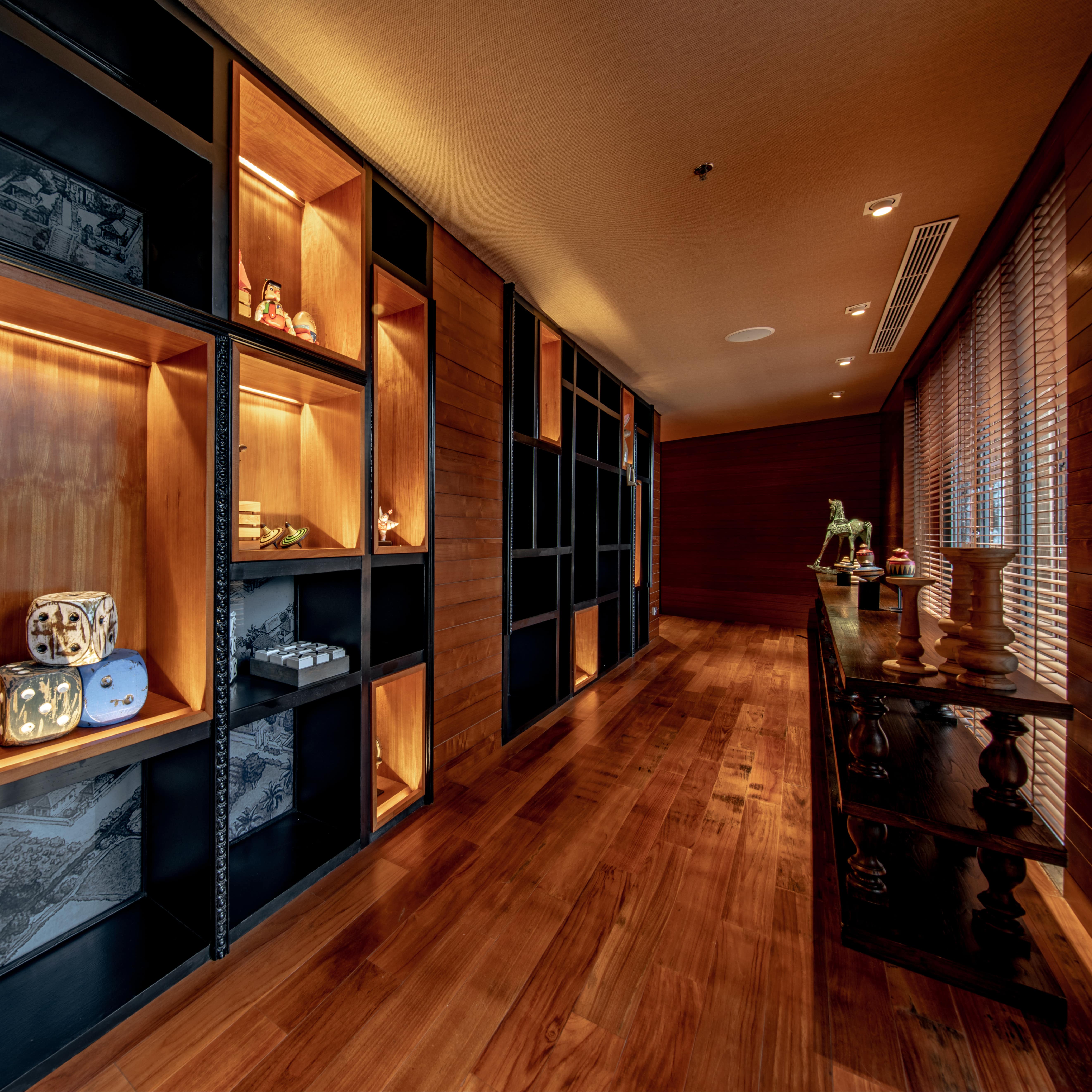Hall of a luxury Bali villa with hardwood floors, built-in shelves with artful decor and a carved wooden shelf by windows