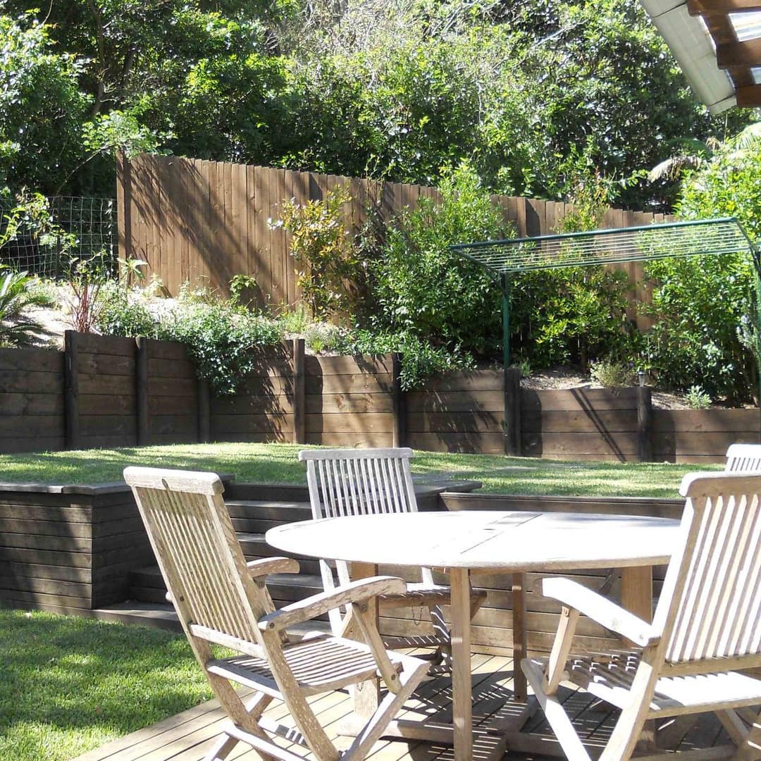 View of a lush, manicured backyard and sunken patio space with a white dining set.