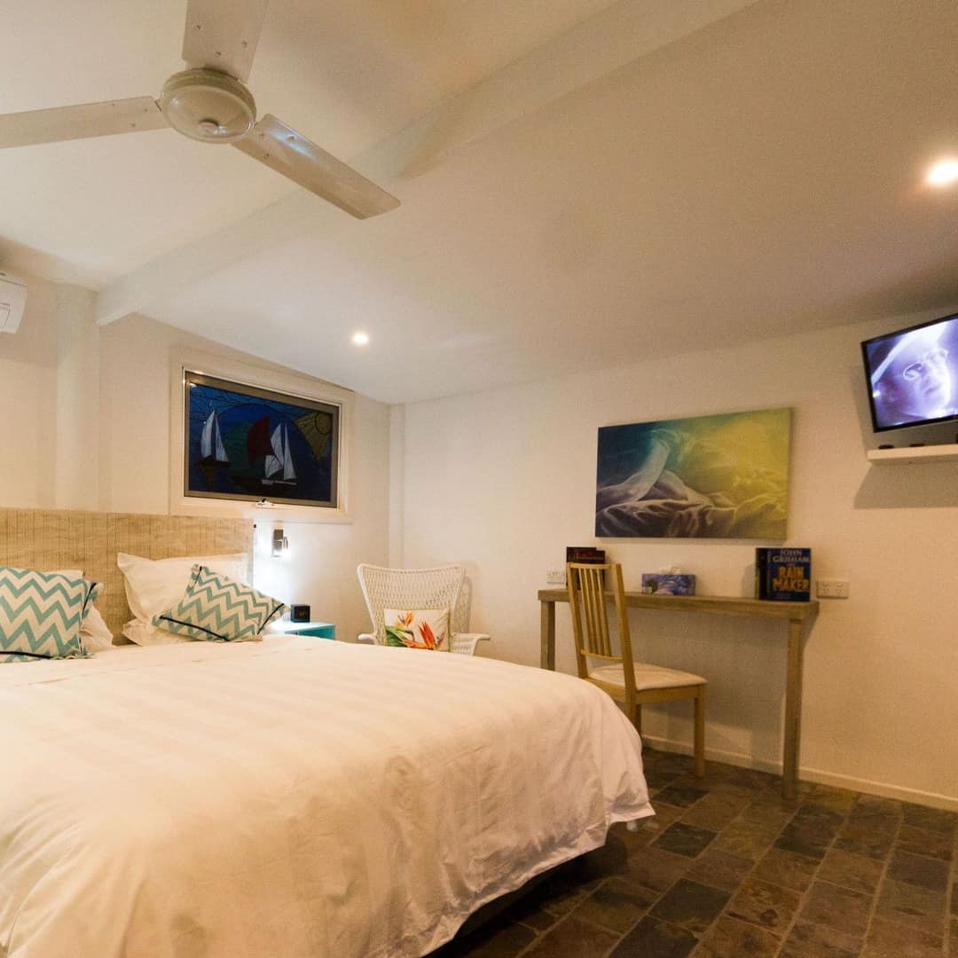 Spacious bedroom with stone floors, white walls, a king size bed, white and blue bedding, and a flatscreen TV.