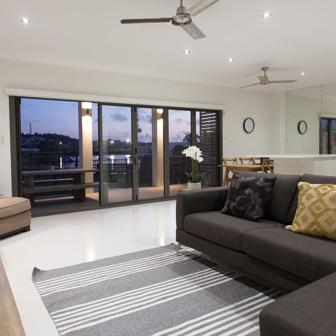 Living room of modern home with gray sectional, rug, and brown chair, and long sliding-glass doors with Cable Park view.