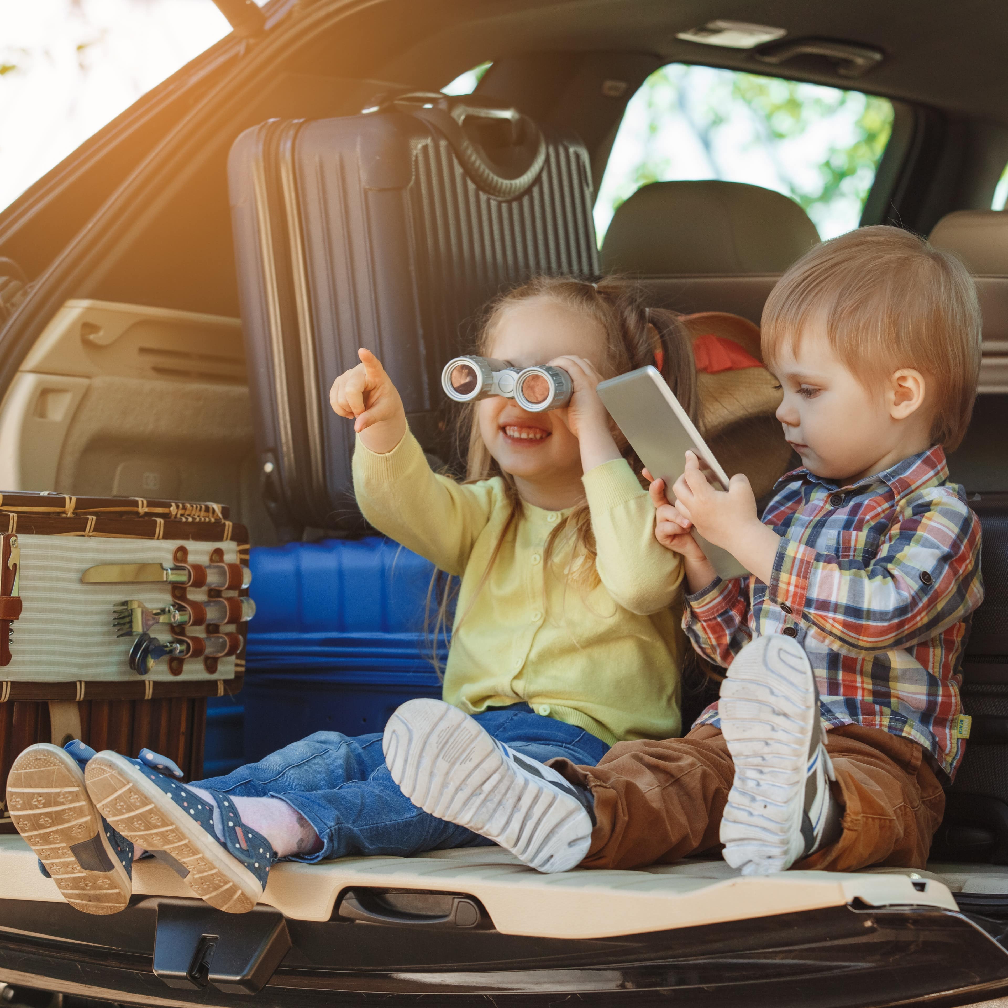 Brother and sister sitting on the tailgate of their SUV packed with luggage for a cross-country trip