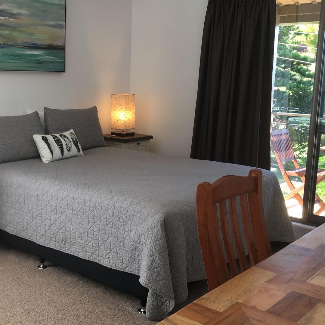 Bedroom with beige carpet and white walls, queen size bed with grey bedding, wood desk, and attached patio.