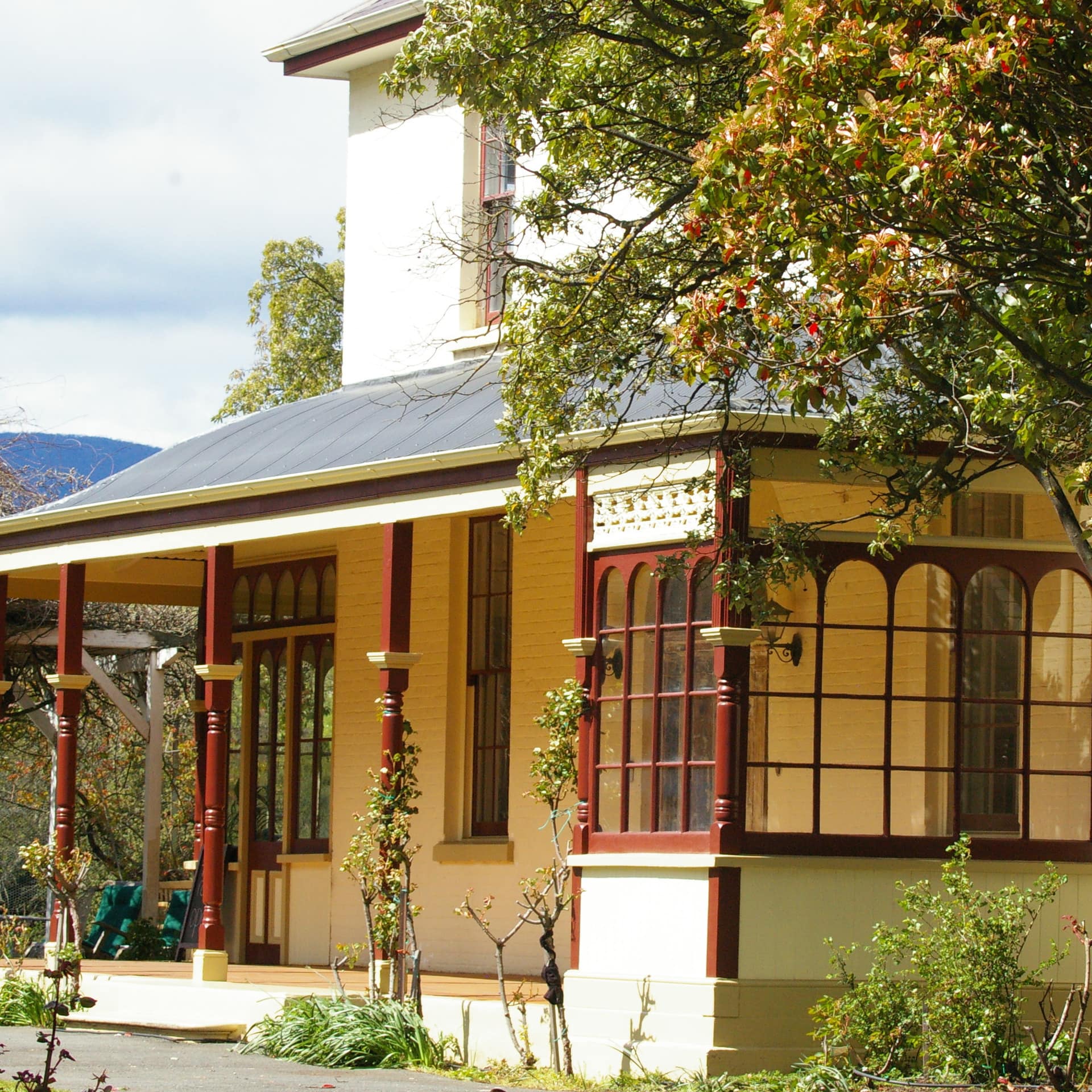 Yellow and burgundy 200-year-old 2-storey Heritage bed and breakfast with lovely front porch and hawthorn tree