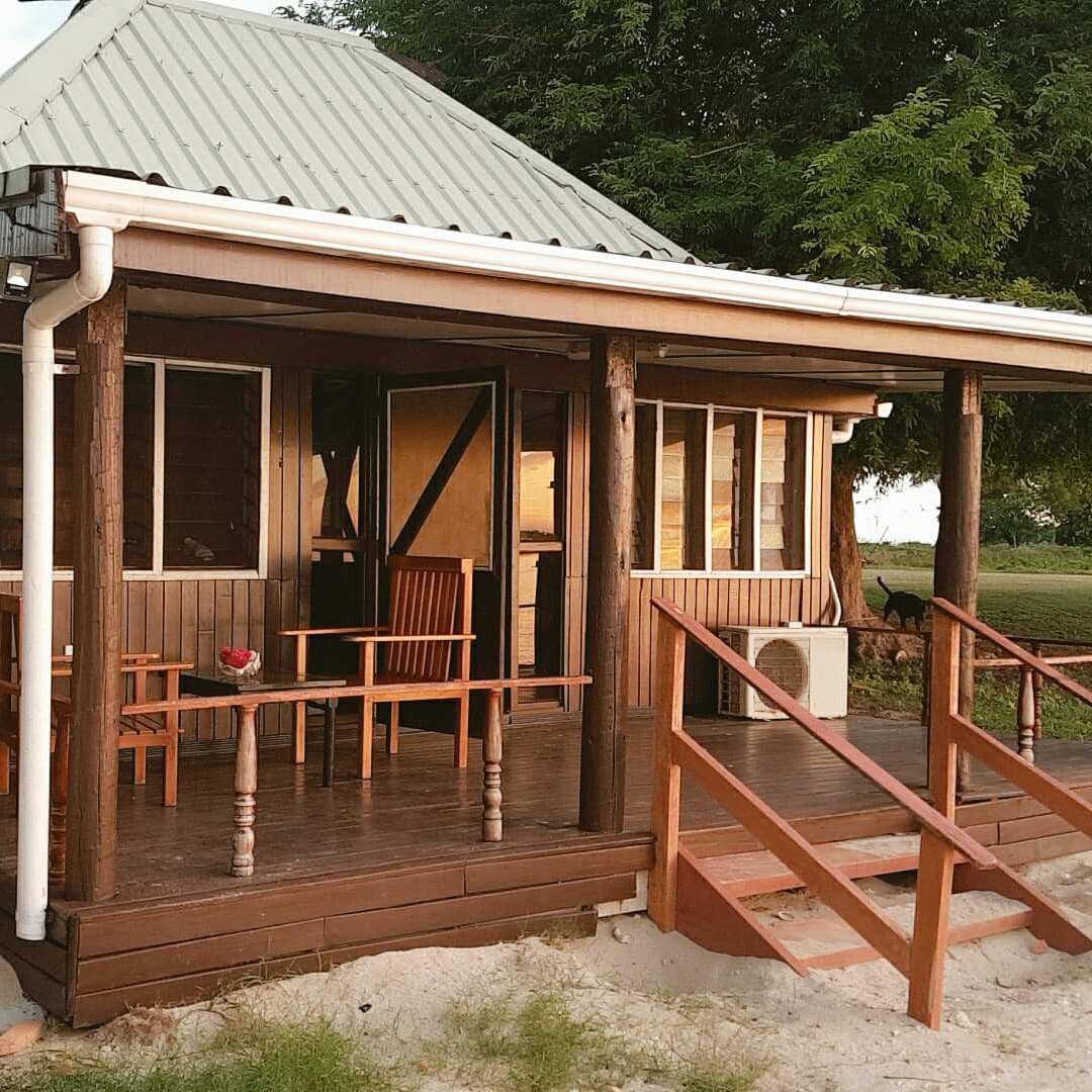 Exterior of a wood cabin with a covered front porch, an outdoor dining set, and a sandy front lawn, surrounded by trees.