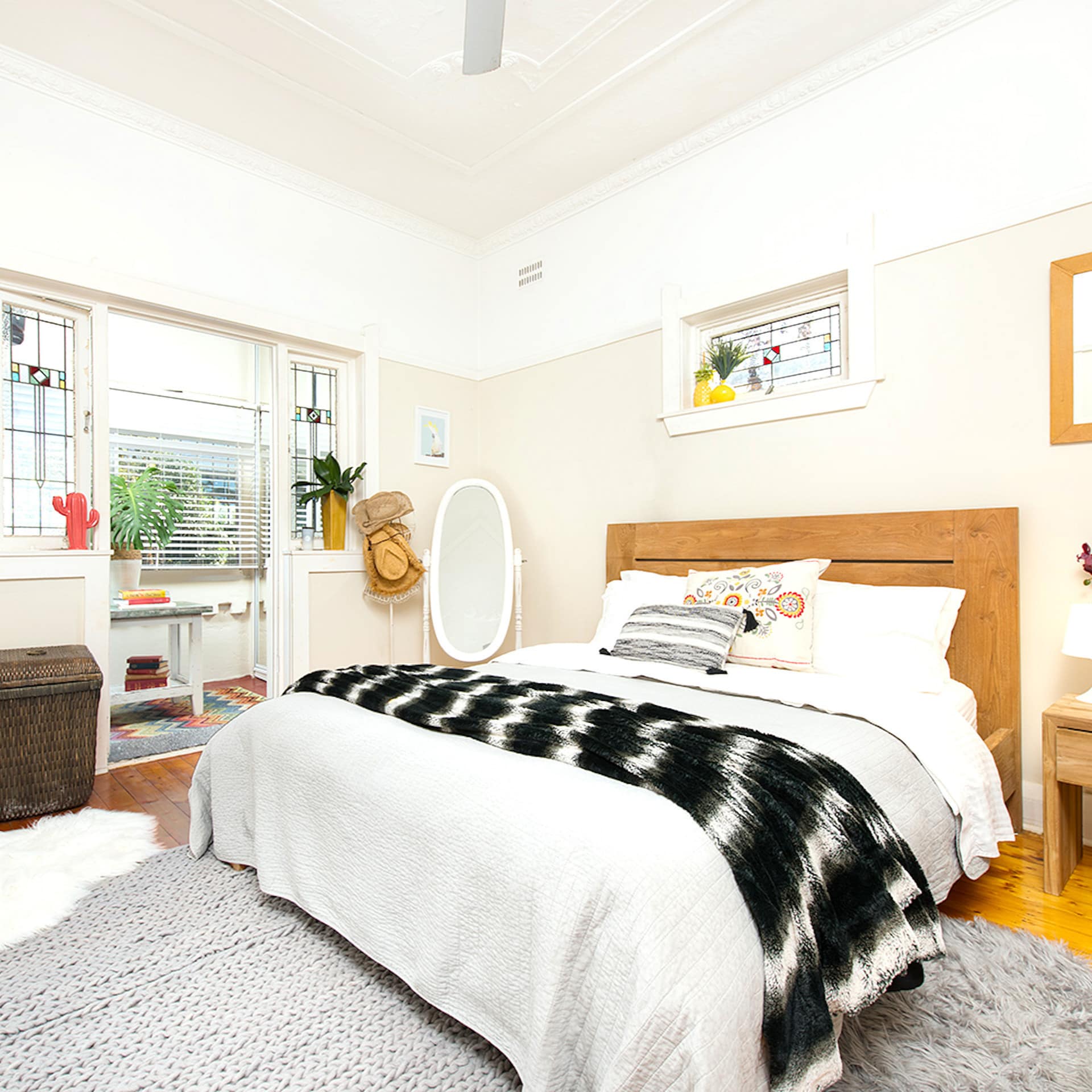 Sunny bedroom with hardwood floors, a king size bed, white and black bedding, grey rug and eclectic decor.