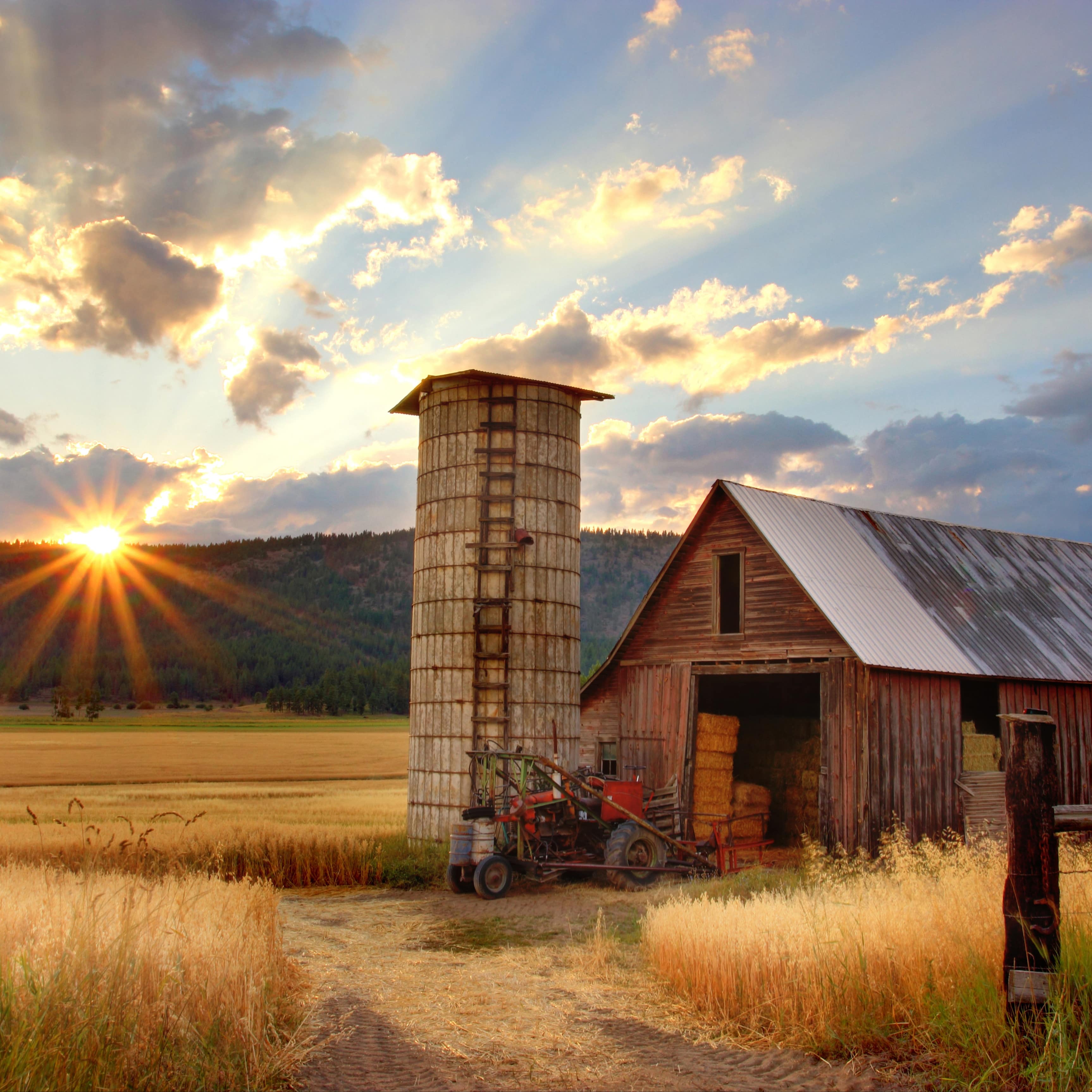 Sun setting over the hills and a dazzling sky with clouds over a barn filled with hay and a granary