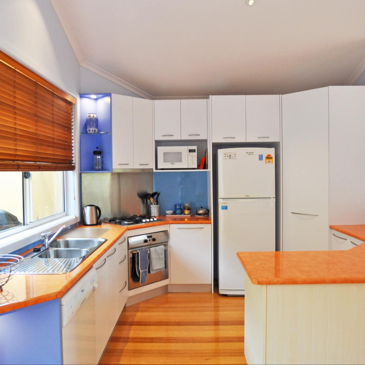 Bright white and blue fully-equiped kitchen with pine wooden floor, blinds and countertops