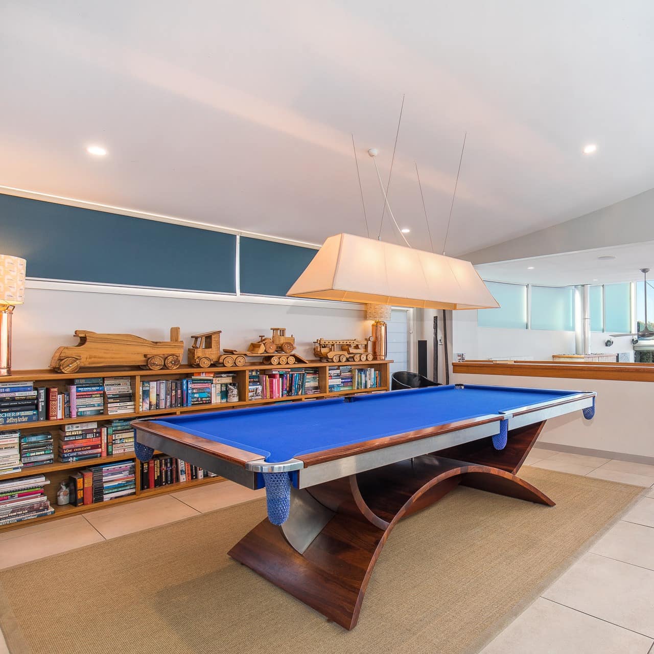 Billiard table and bookshelves, with stairs leading down to a sitting area that is open to the outdoors and overlooks the sea 