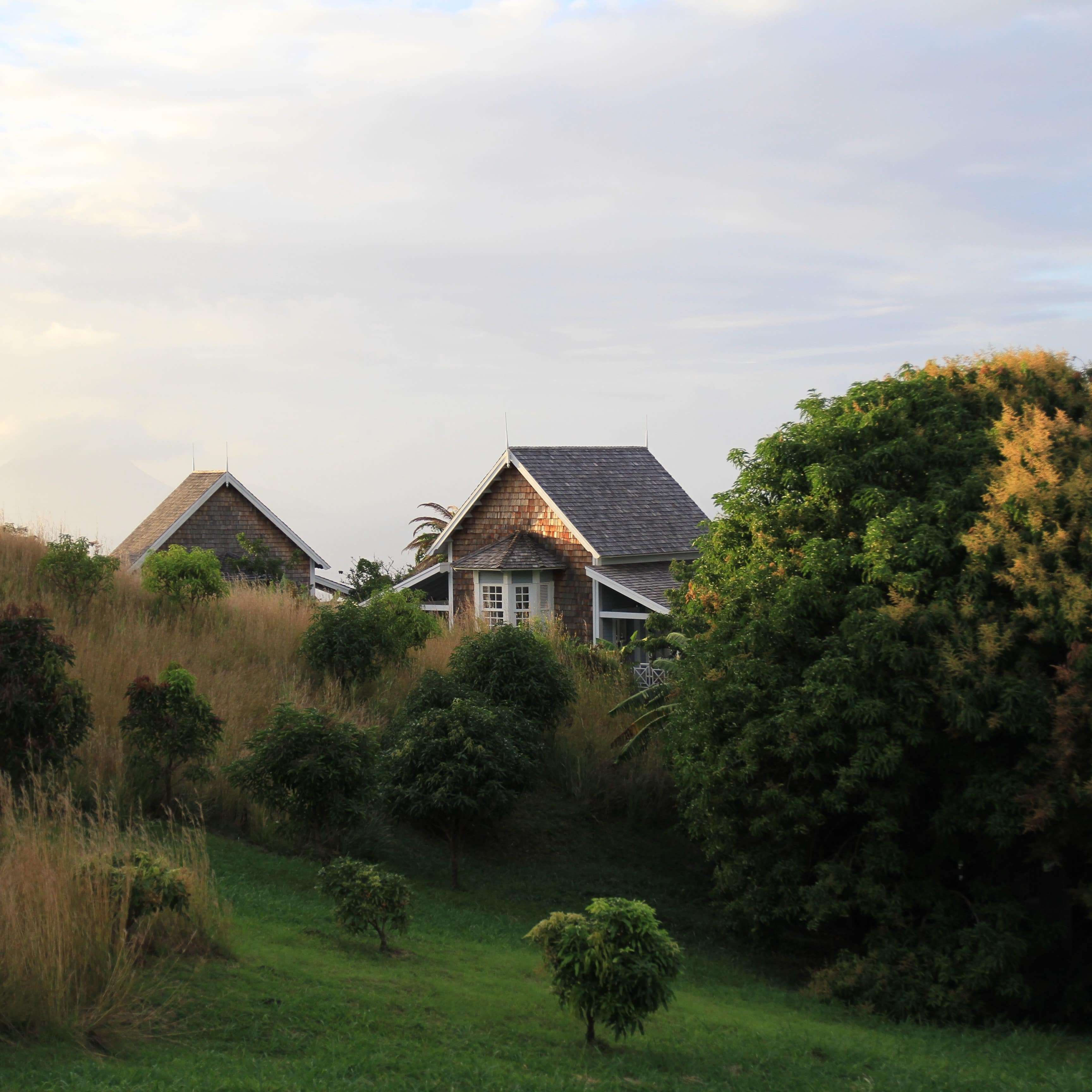 Cottages with a veranda on either side and shake shingles set on a hillside with grasses and trees