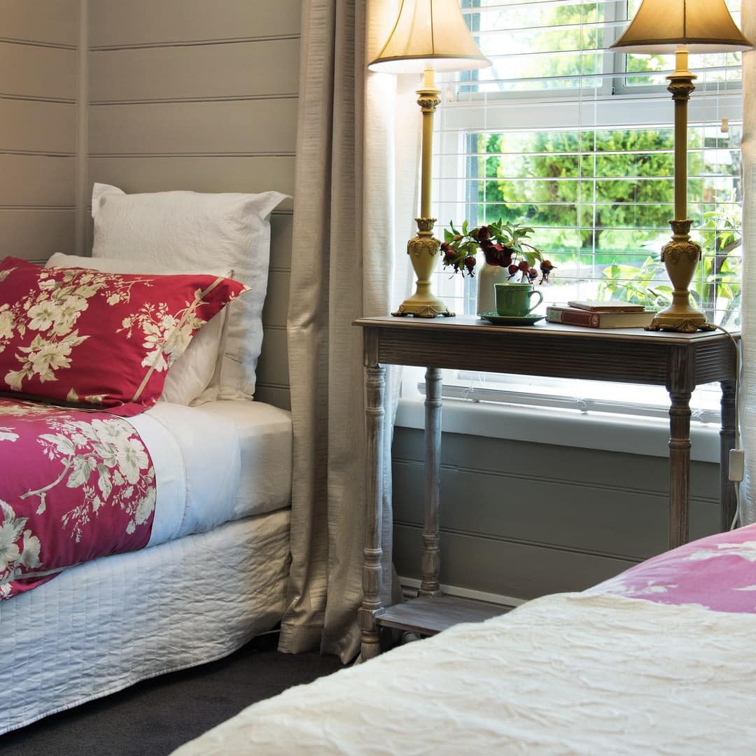 Bedroom with tan walls, two twin beds, red floral bedding, and a tall window with beige curtains.