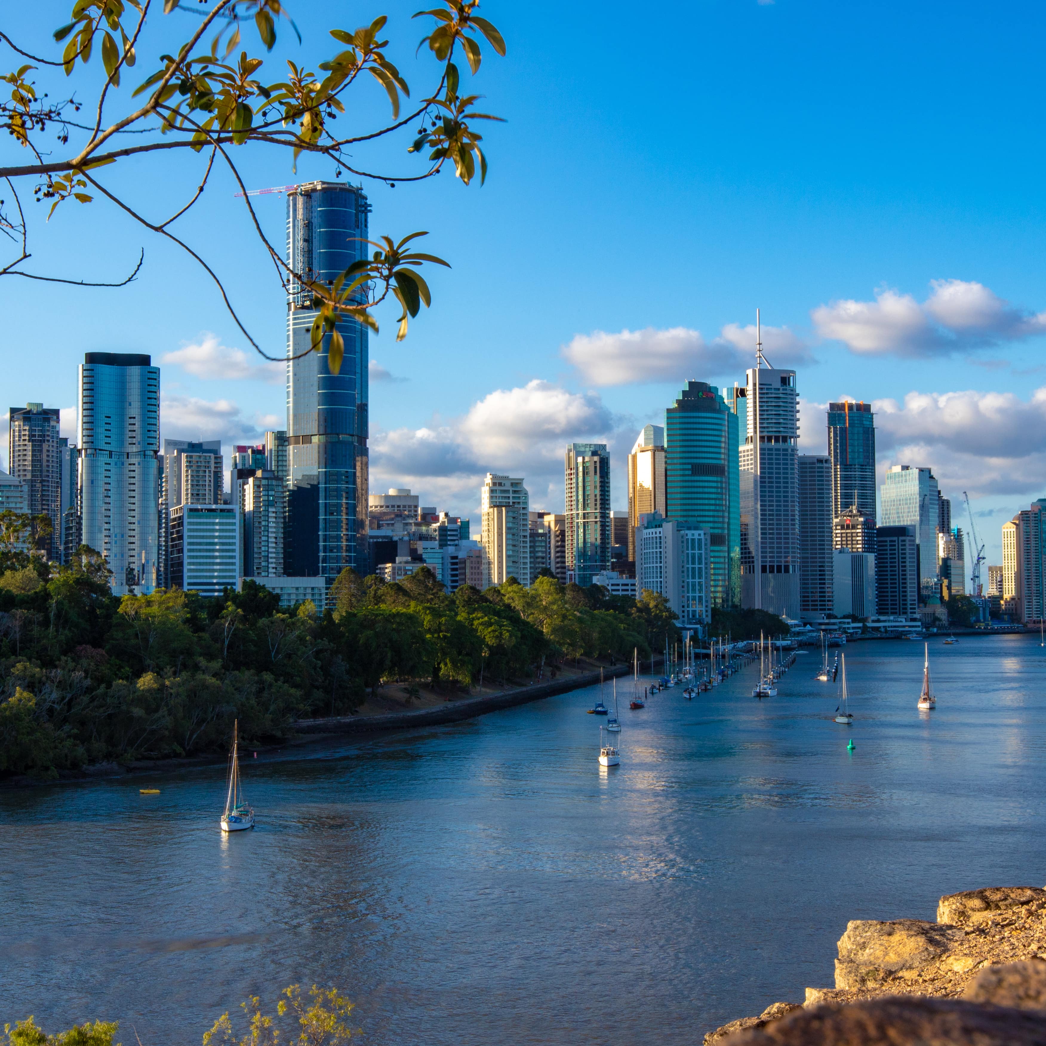A view of Brisbane and the river from Kangaroo Point Cliffs with sailboats on the water at sunrise and the city skyline