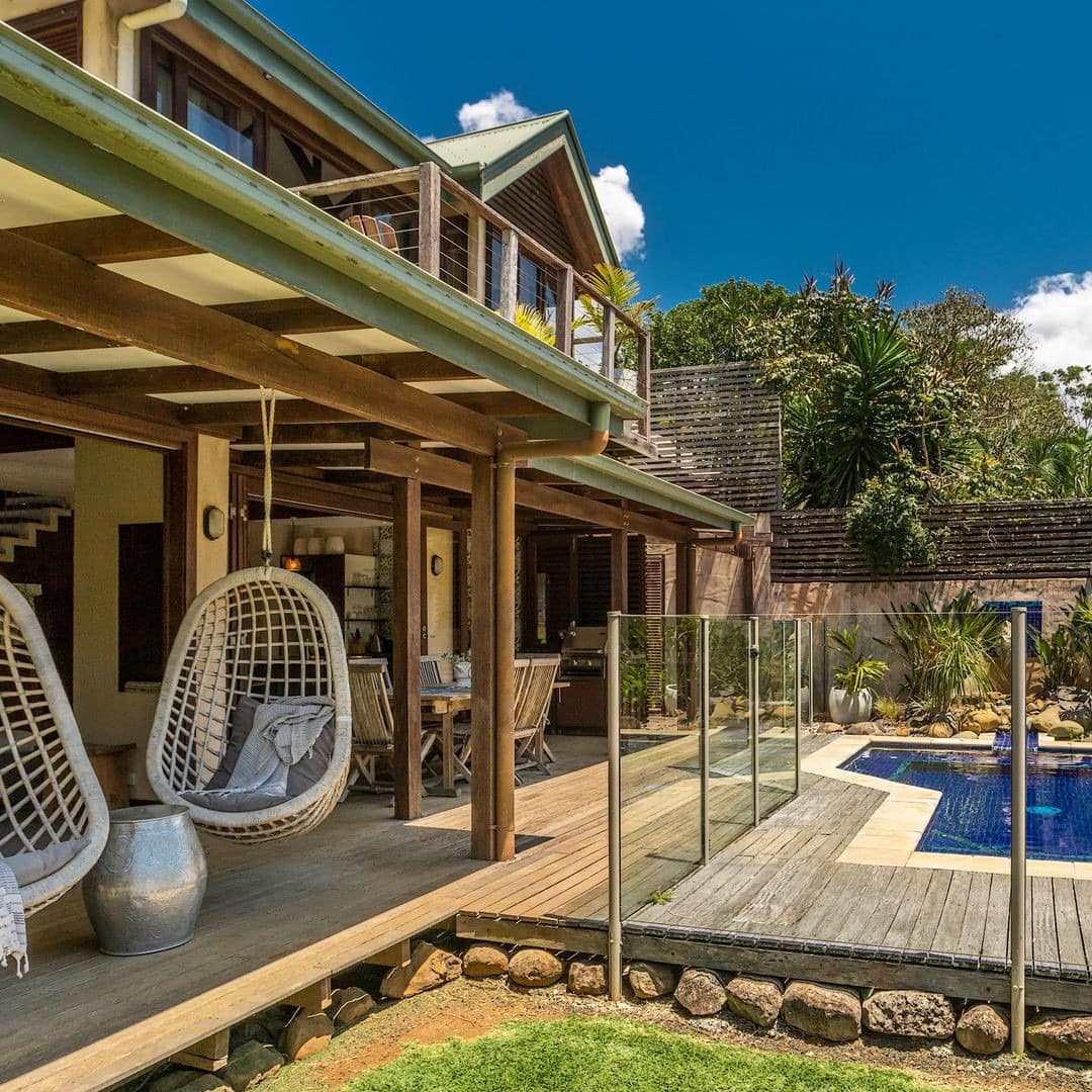 Exterior view of spacious, raised, wooden patio with private pool, hanging rattan chairs, surrounded by tropical vegetation.