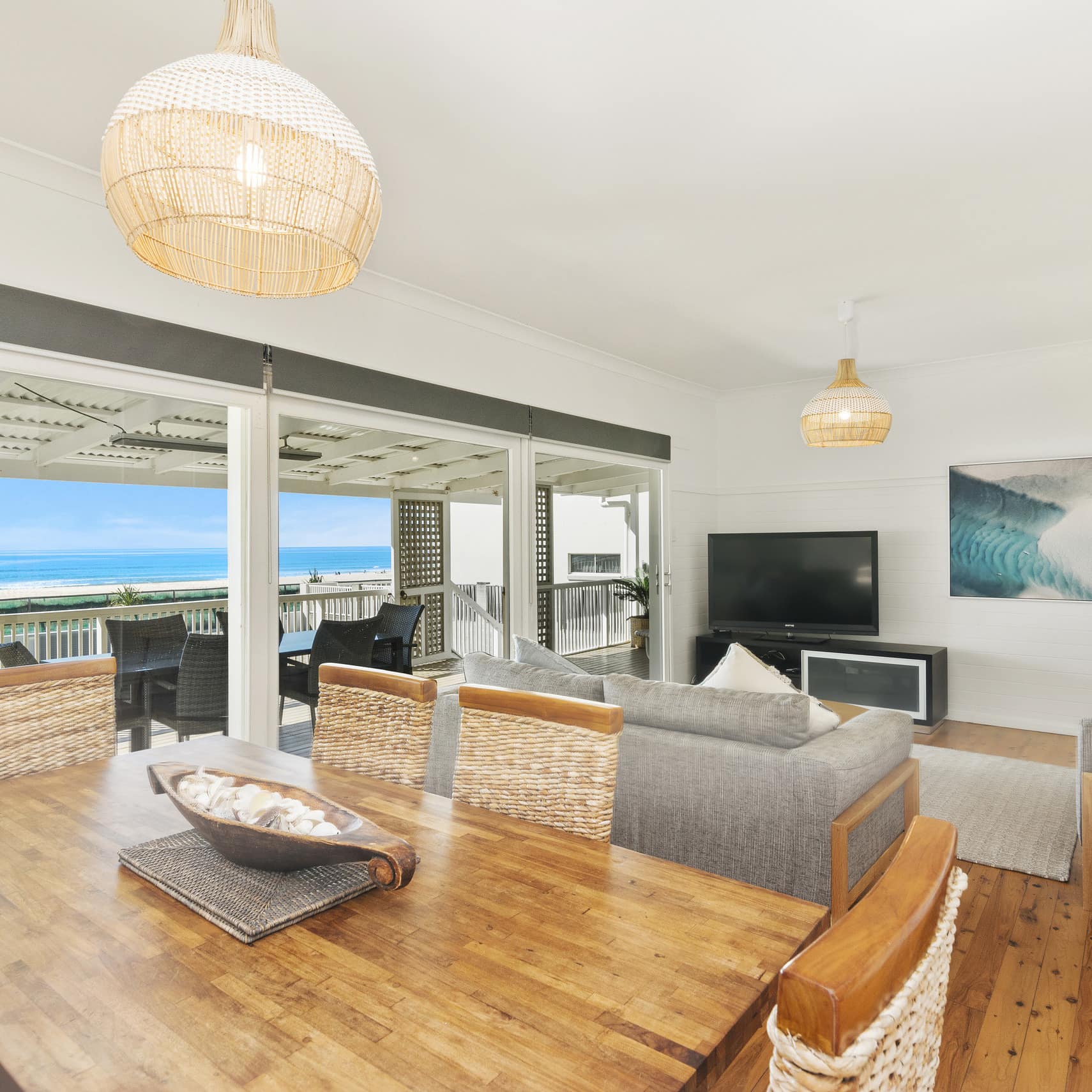 Living and dining area in Gold Coast beachfront 3BR house with wicker-backed dining chairs, hardwood floors and beach view