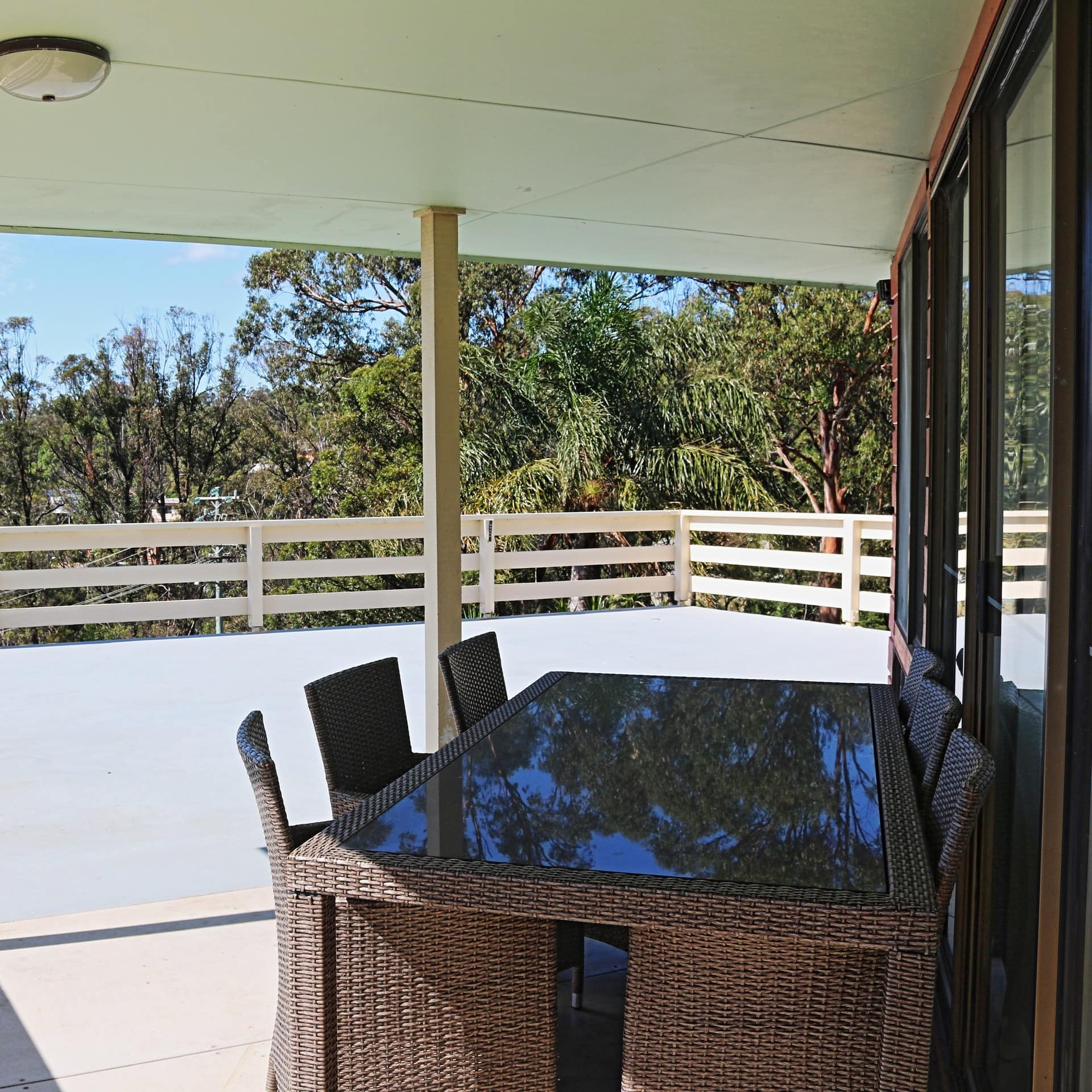 Spacious covered deck overlooking lush lawn and trees, brown wicker dining table set.