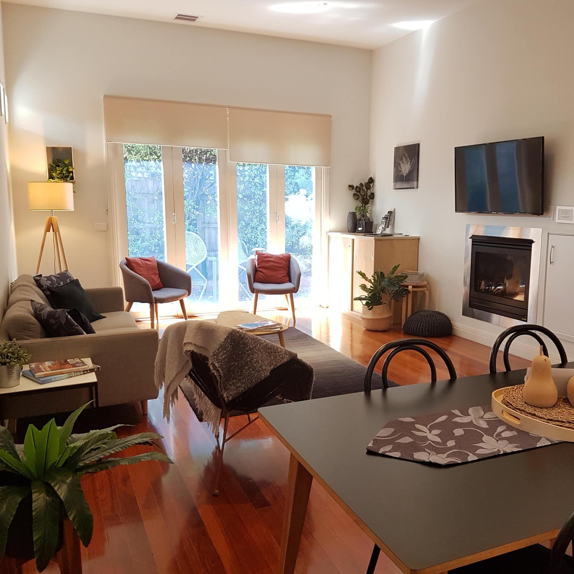 Living and dining area of historic Magnolia House with modern warm, gray furnishings, wood floors, fireplace and TV.