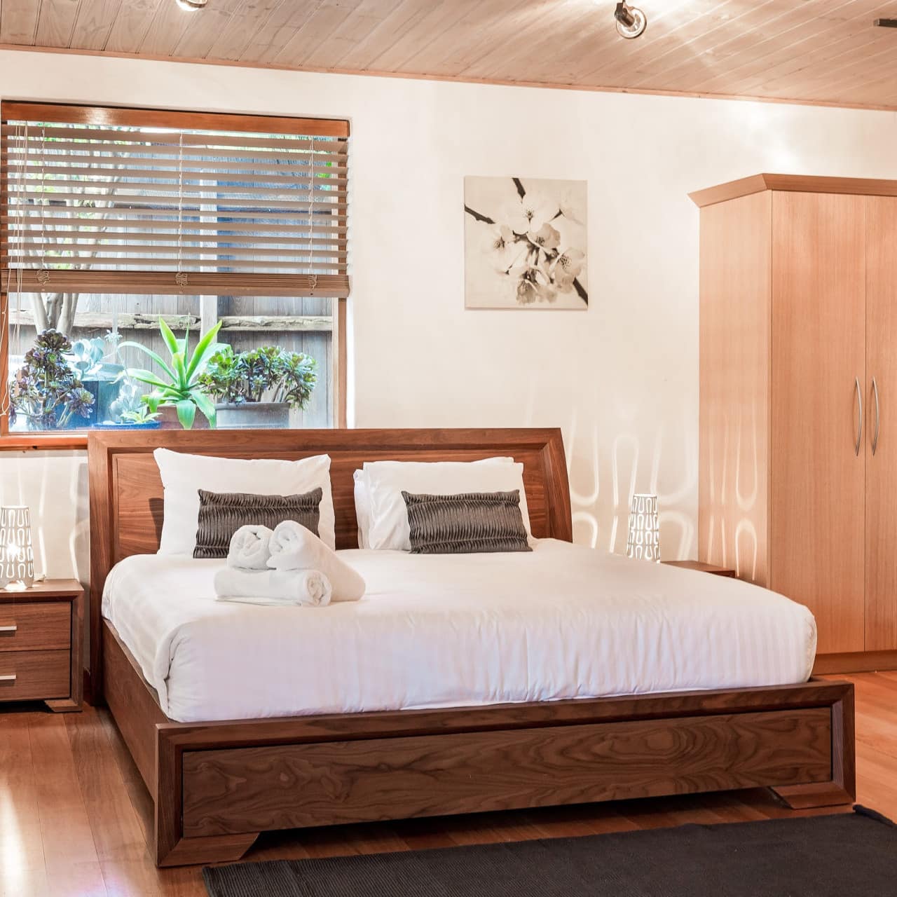 A bedroom with hardwood floors, white walls, a wood-framed king size bed, white bedding, and large wooden wardrobes.