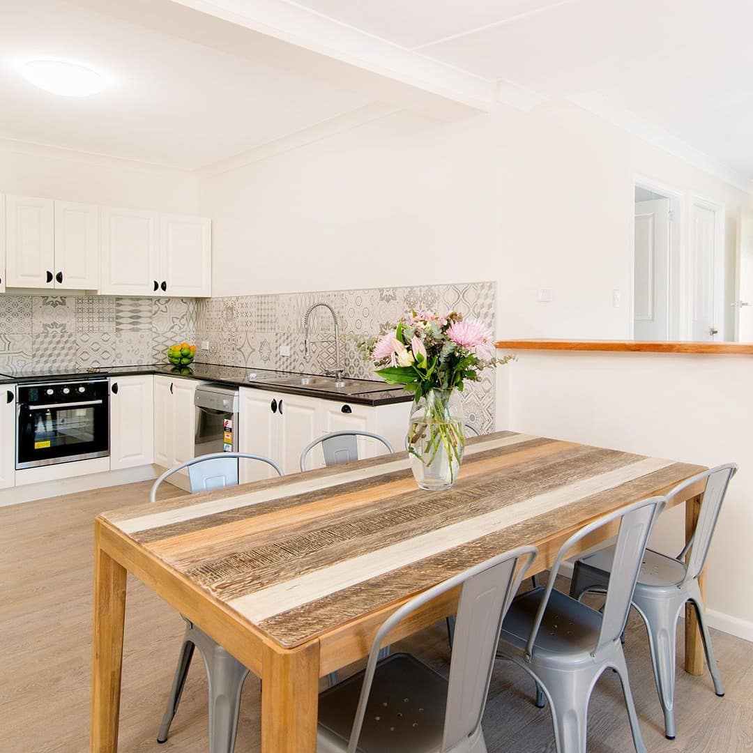 Open kitchen and dining room, hardwood floors, white walls, rustic dining set with reclaimed wood table and metal chairs.