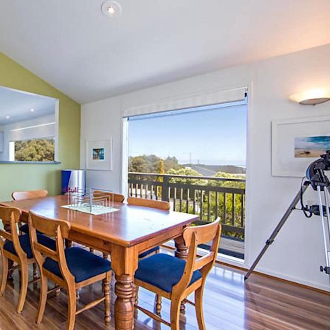 Open dining room with hardwood floors, a green accent walls, wooden dining set, and wide windows.